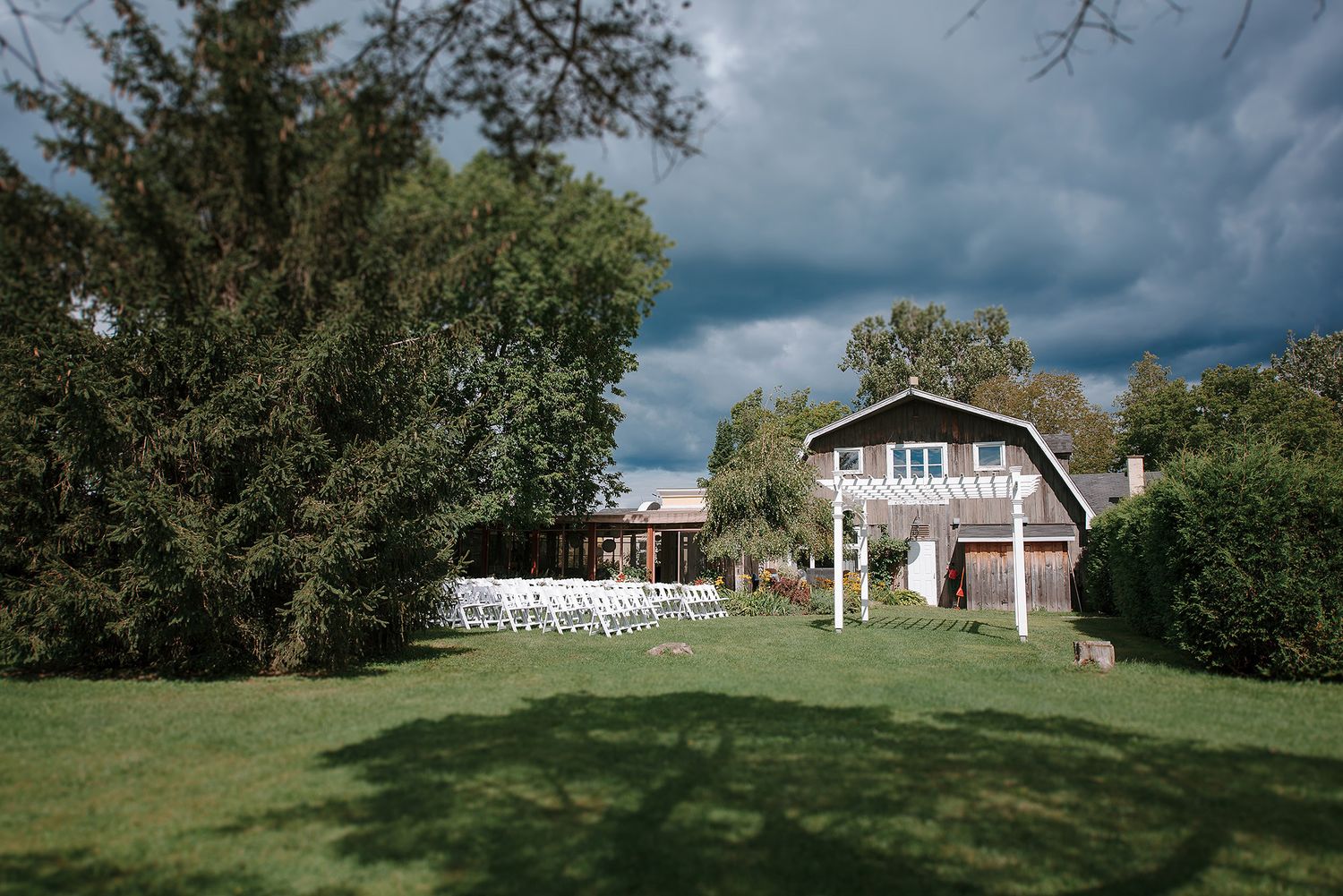 Panoramic view of rustic buildings and green landscape under dramatic cloudy skies.