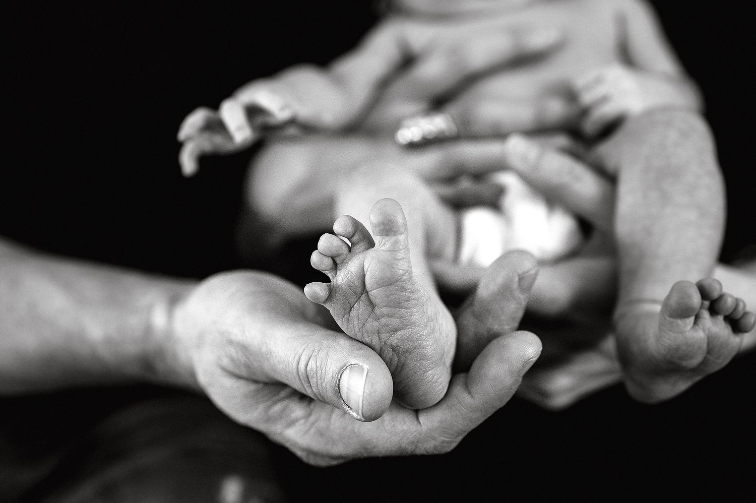 Close-up black and white photos of gentle hands holding newborn.