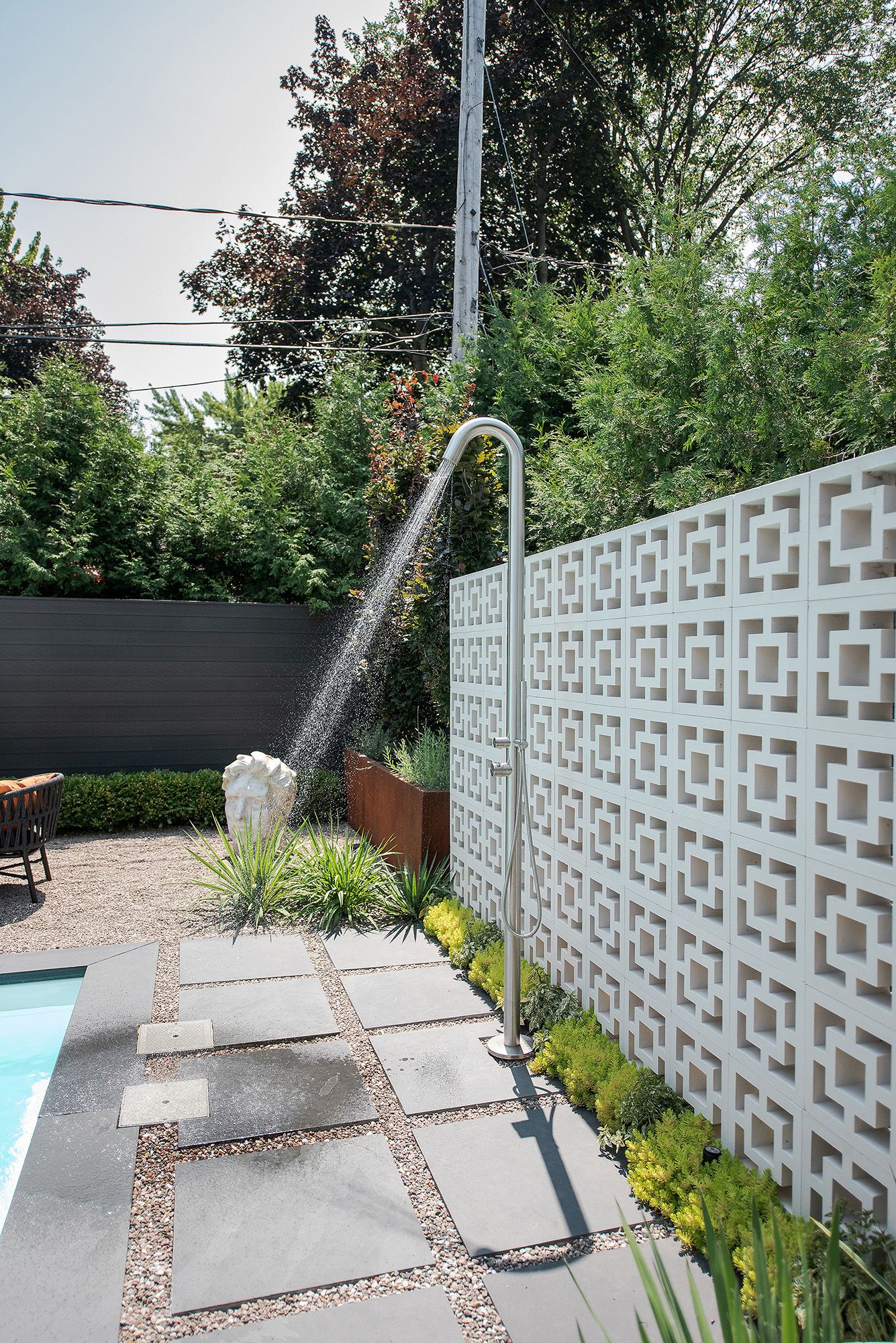A modern outdoor patio features a white geometric breeze block wall and concrete pavers with gravel accents.
