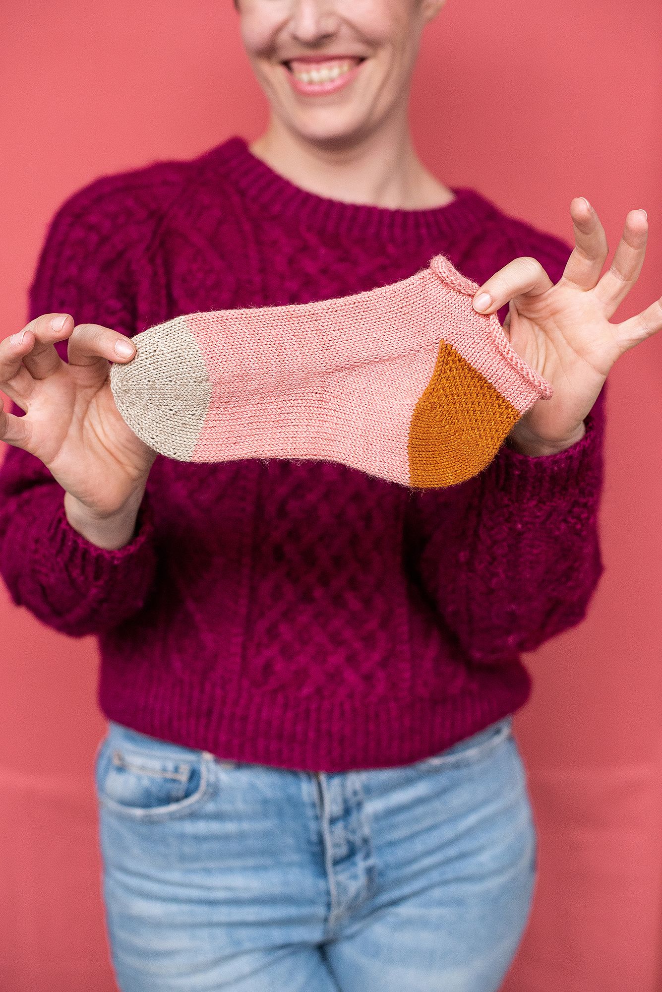Knitted pink and orange sock being displayed against coral colored background.