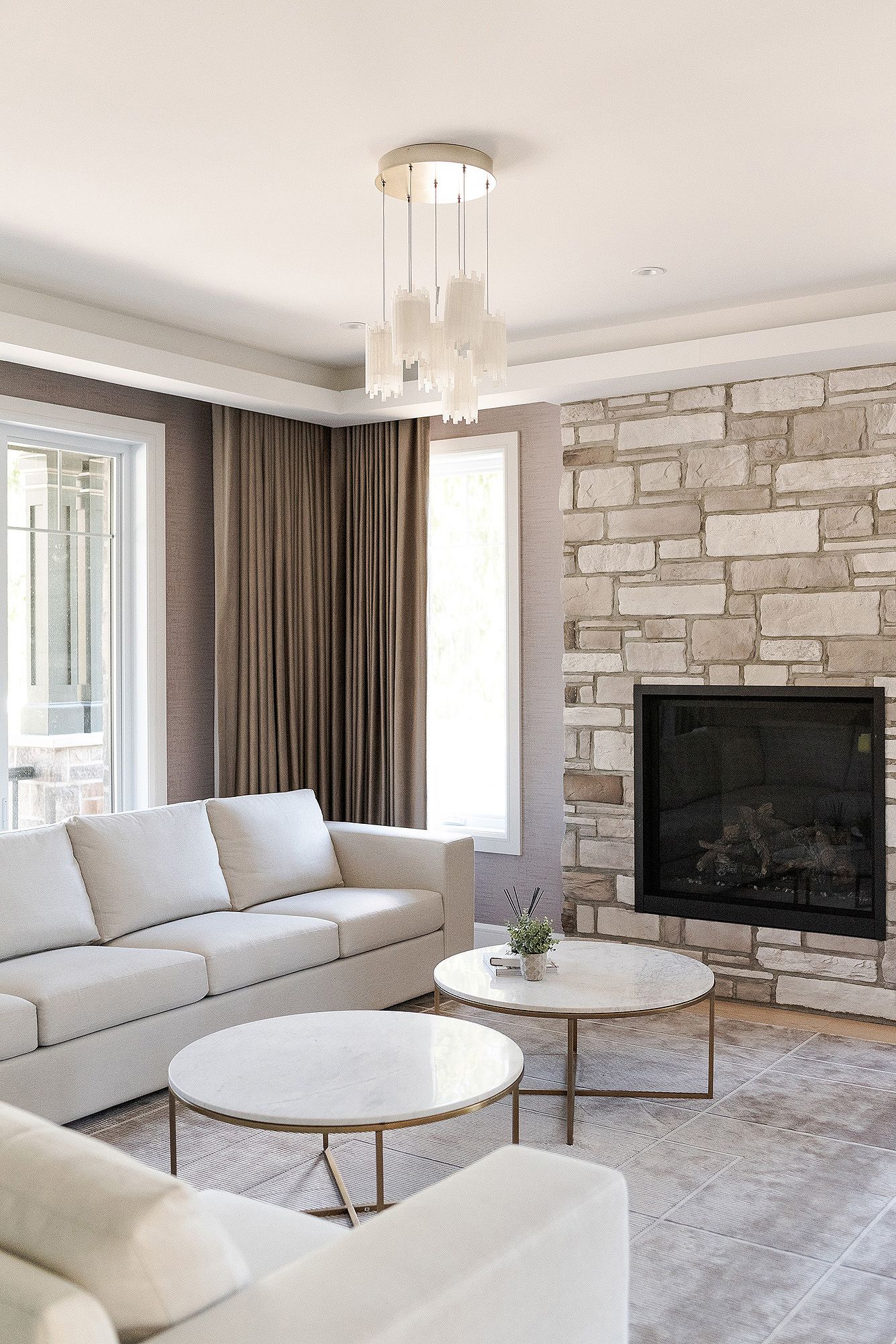 Modern living room with stone accent wall, white sectional sofa, round coffee table and contemporary pendant lighting.