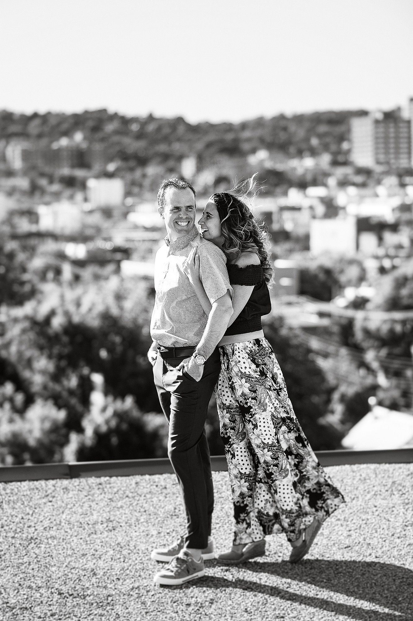 Couple dancing and twirling together on a rooftop with a cityscape backdrop in black and white.