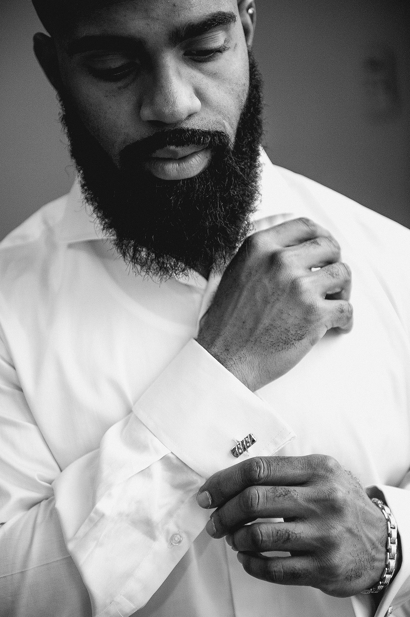 Dapper groom fastening cufflinks on white dress shirt in elegant black and white photo.