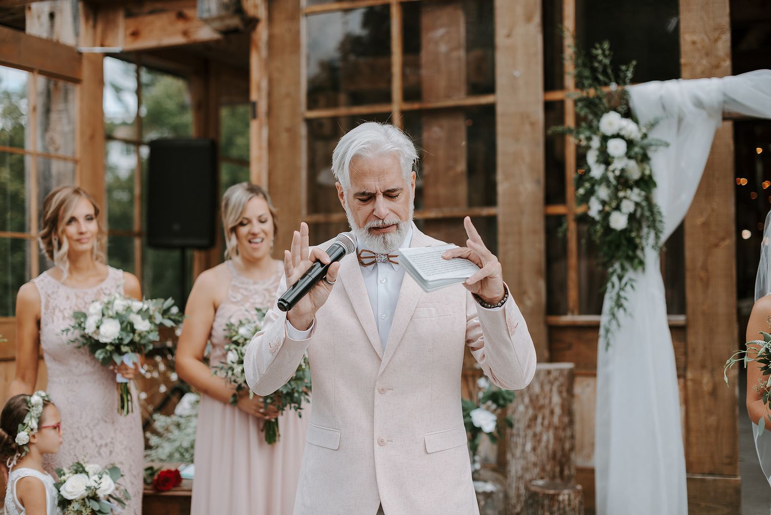 A rustic wooden wedding venue with white floral decorations and people gathered for a celebration.