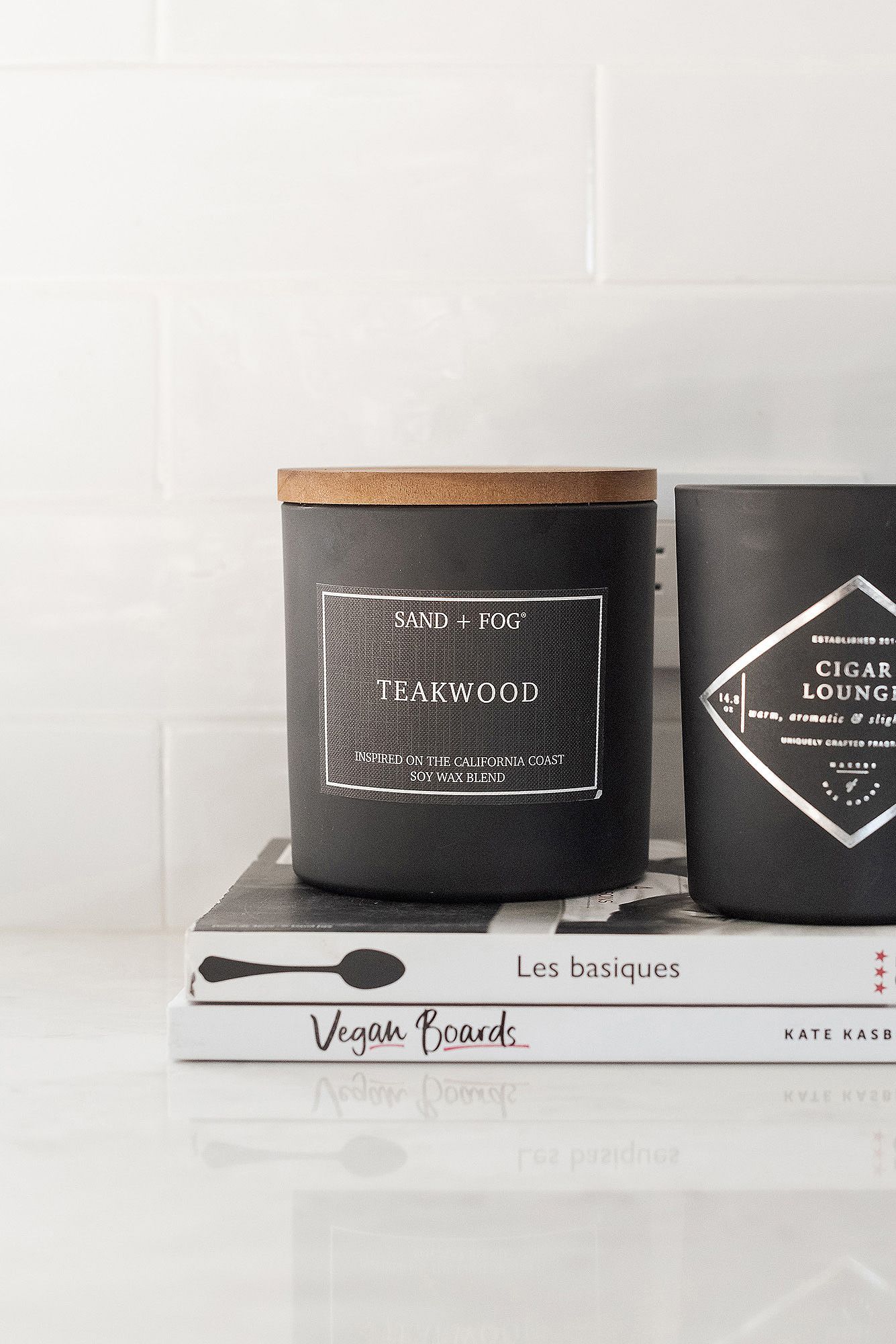 Collection of elegant black scented candles with minimalist labels including Teakwood and Sand & Fog fragrances.