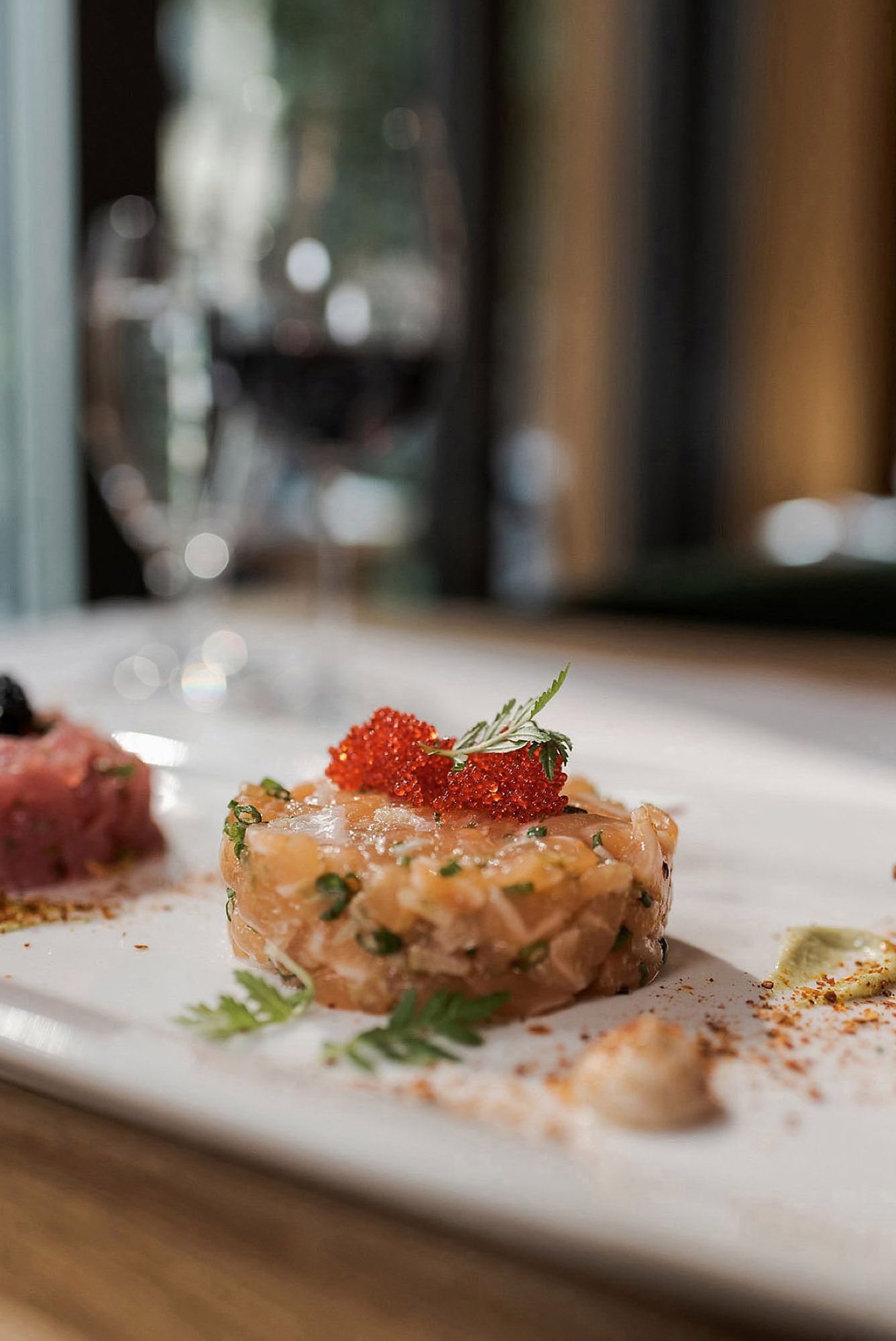 Elegant plated appetizers featuring salmon tartare with red caviar and fresh herbs arranged in a linear presentation.