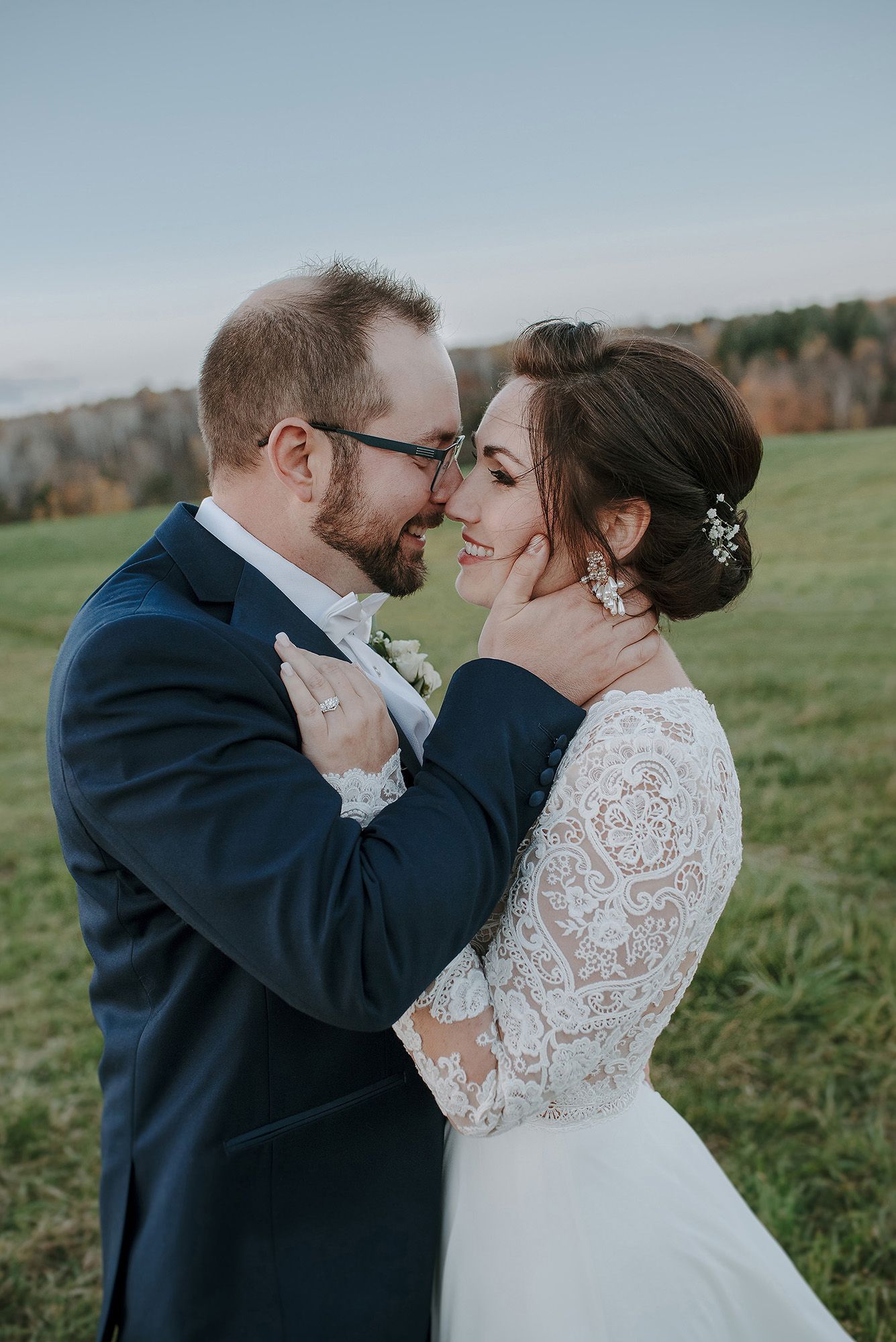 Romantic wedding couple embraces in a lush green field on an overcast autumn day.