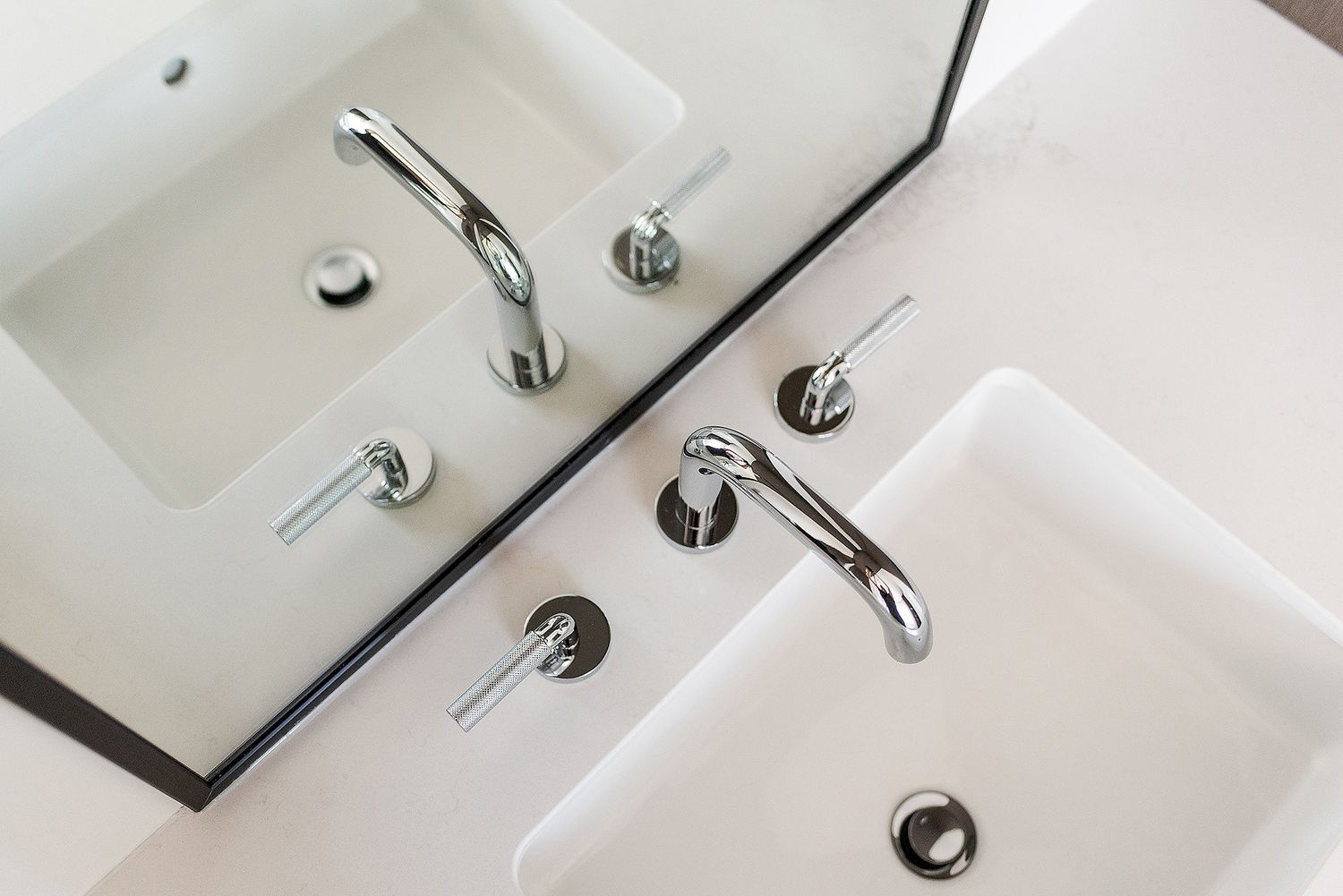 Close-up view of modern chrome bathroom faucets and white porcelain sinks in a row.