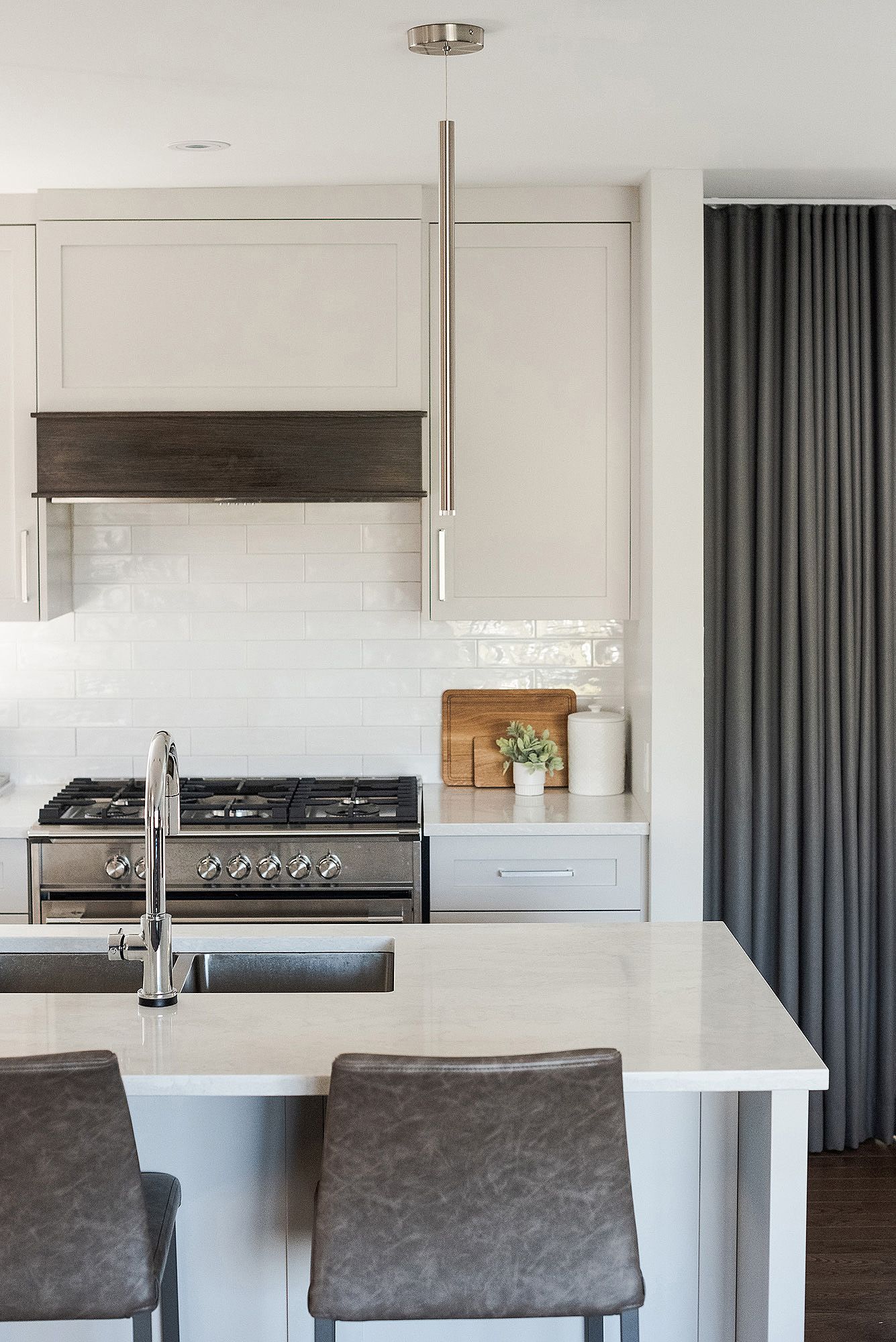 Modern kitchen interior with gray bar stools and white countertops featuring sleek pendant lighting and stainless appliances.