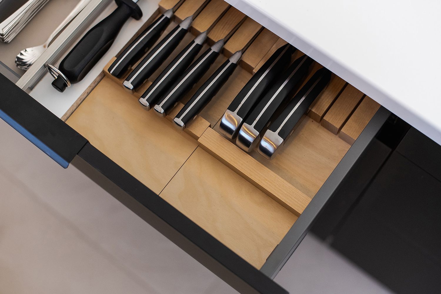 Organized knife drawer insert showing black-handled knives stored neatly in wooden slots.