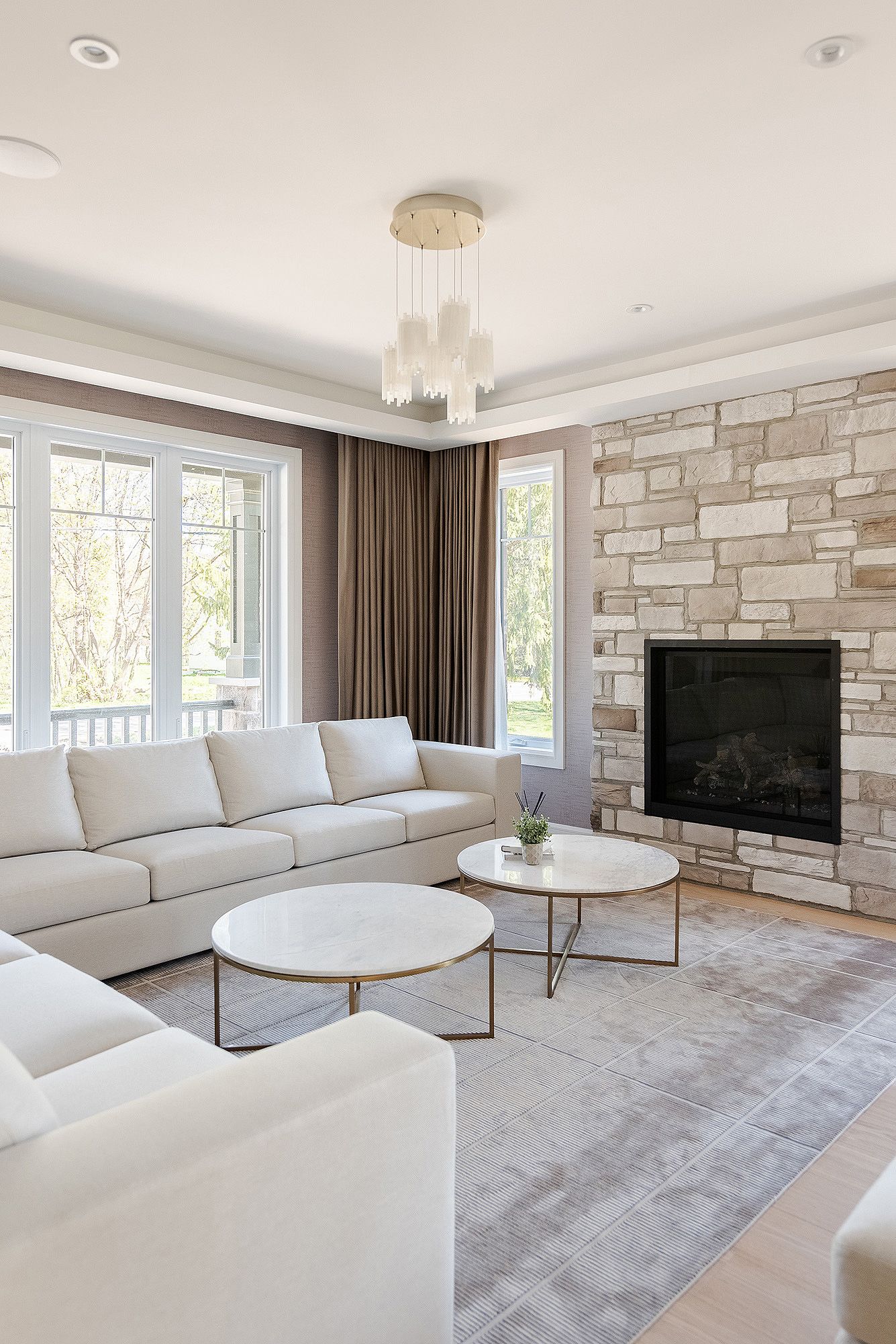 Contemporary white living room with stone accent wall, modern furniture, and large windows letting in natural light.