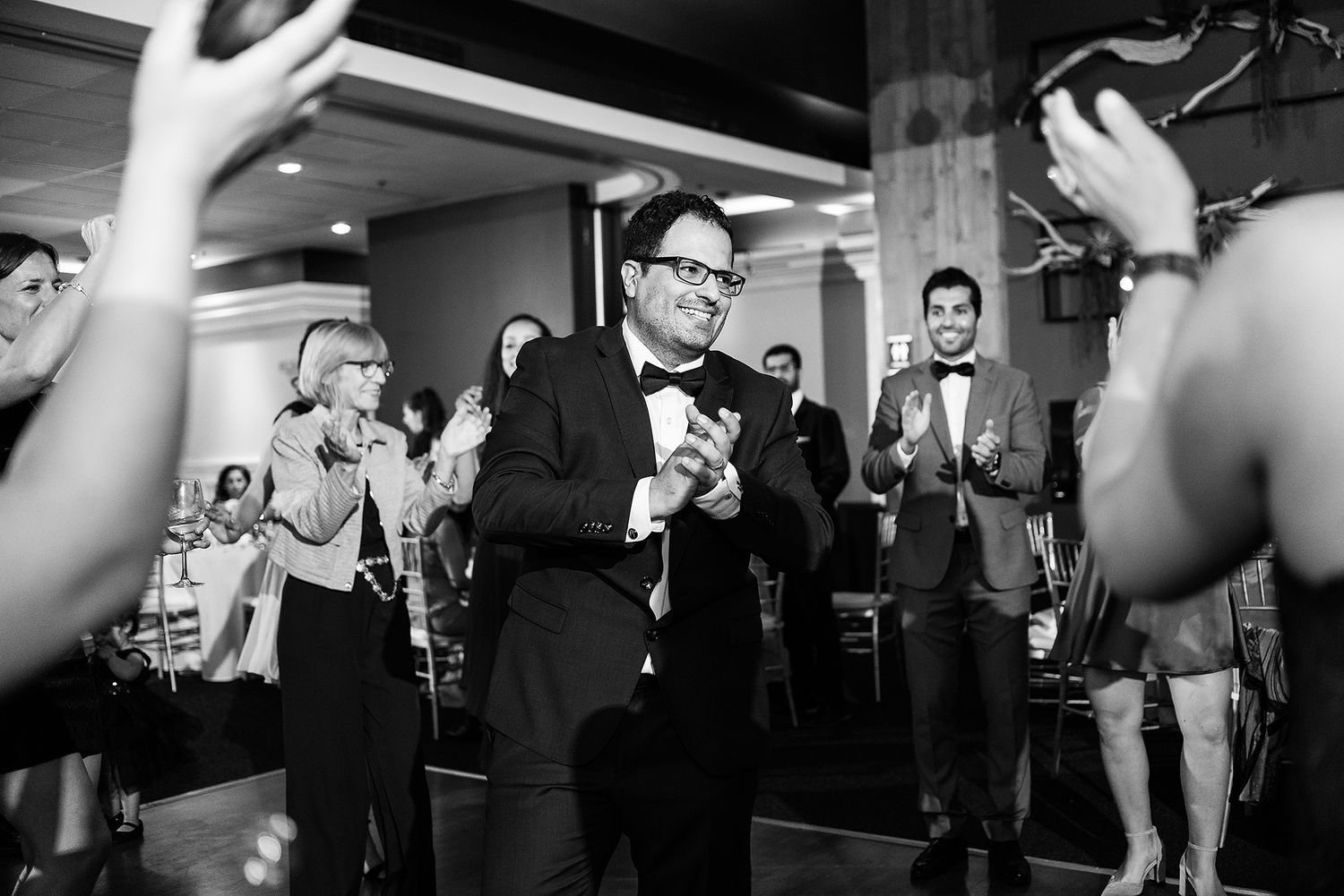Black and white photo of guests dancing and celebrating at a lively wedding reception party.