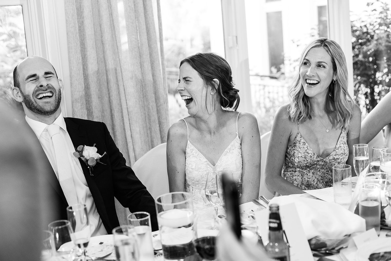 A series of candid black and white wedding reception photos showing guests laughing and enjoying themselves at tables.