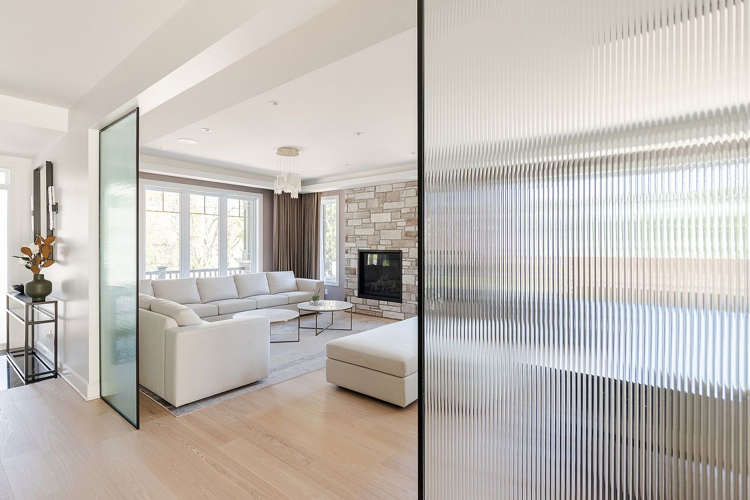 Modern living room with white sofa and fluted glass partition wall featuring natural light and stone accent wall.