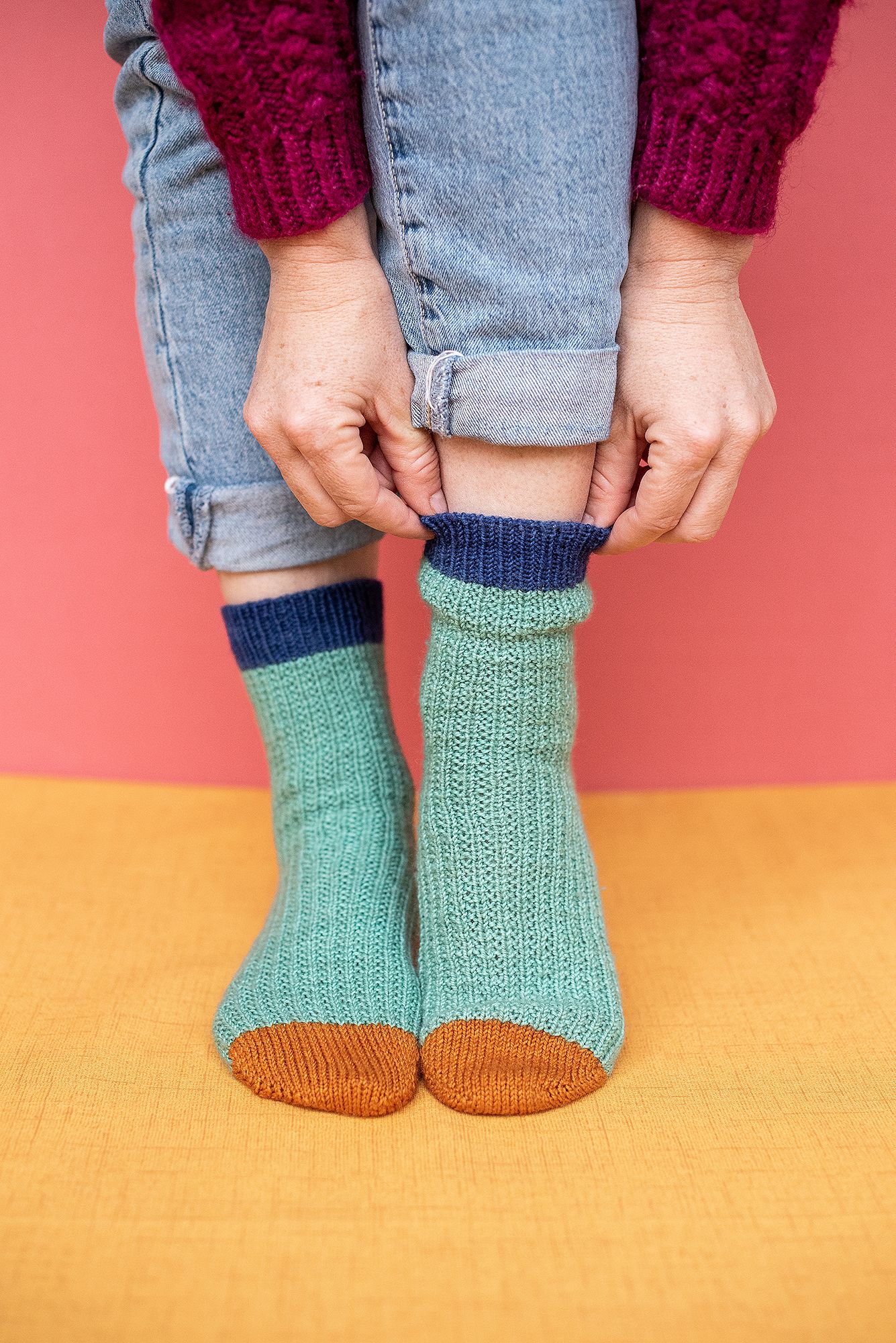 Feet wearing mint green knitted socks with brown toes against coral and yellow background.