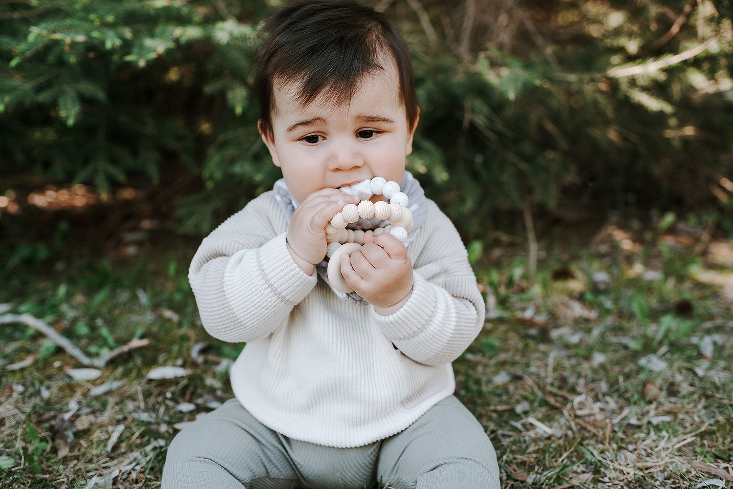 Baby in white sweater sitting on ground exploring with a curious expression.