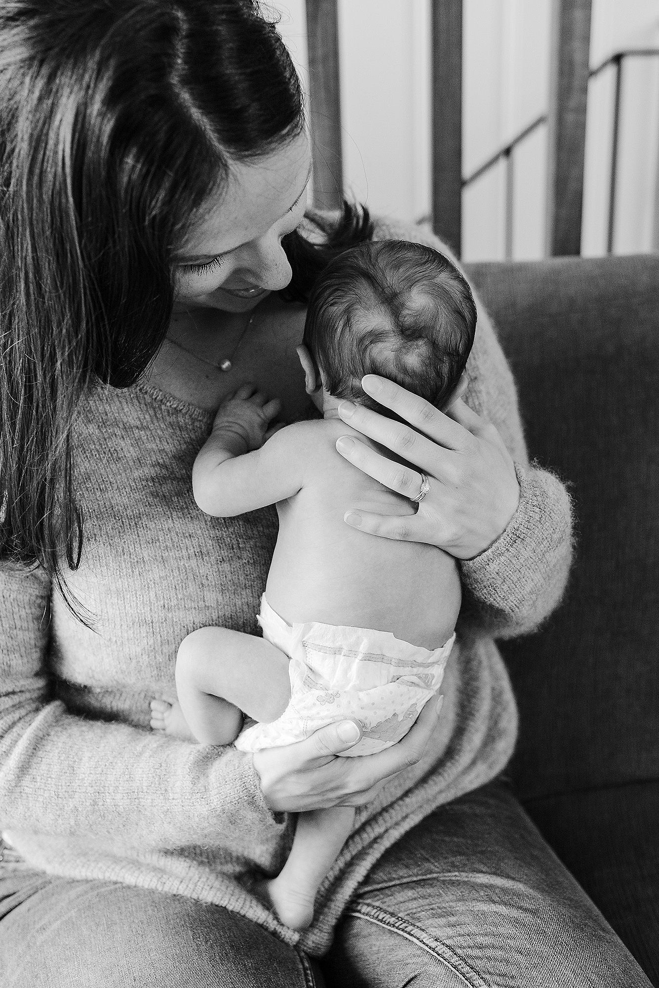 A tender black and white photograph showing an intimate moment between parent and infant in a cozy home setting.