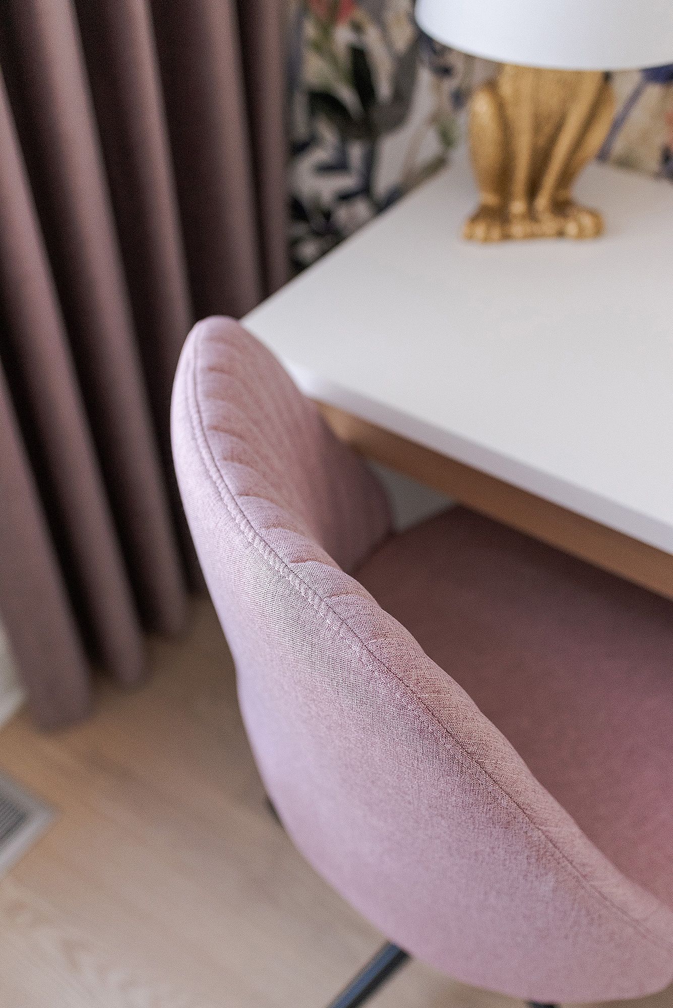 Close-up view of a dusty pink velvet armchair showing curved backrest details against brown curtains.