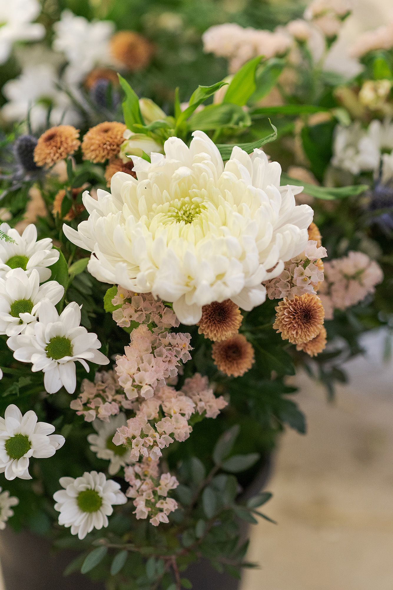 A delicate floral arrangement featuring white chrysanthemums and pink blooms with brown accents in natural lighting.