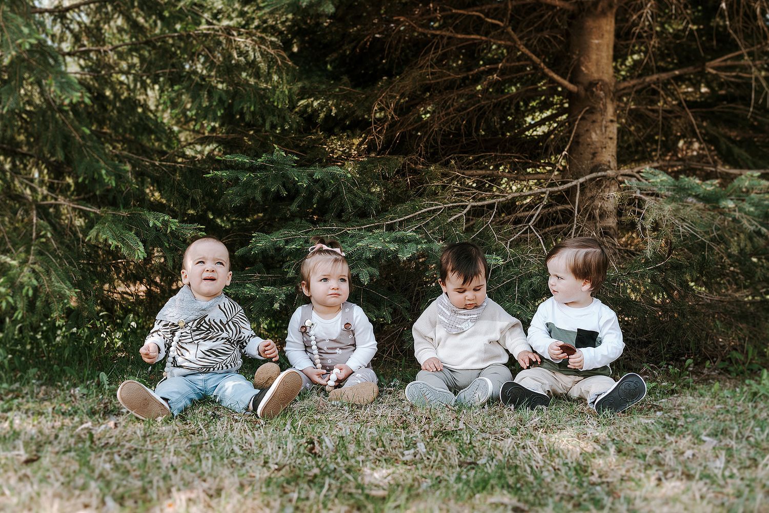 Children arranged in playful poses while sitting on grass near evergreen trees.