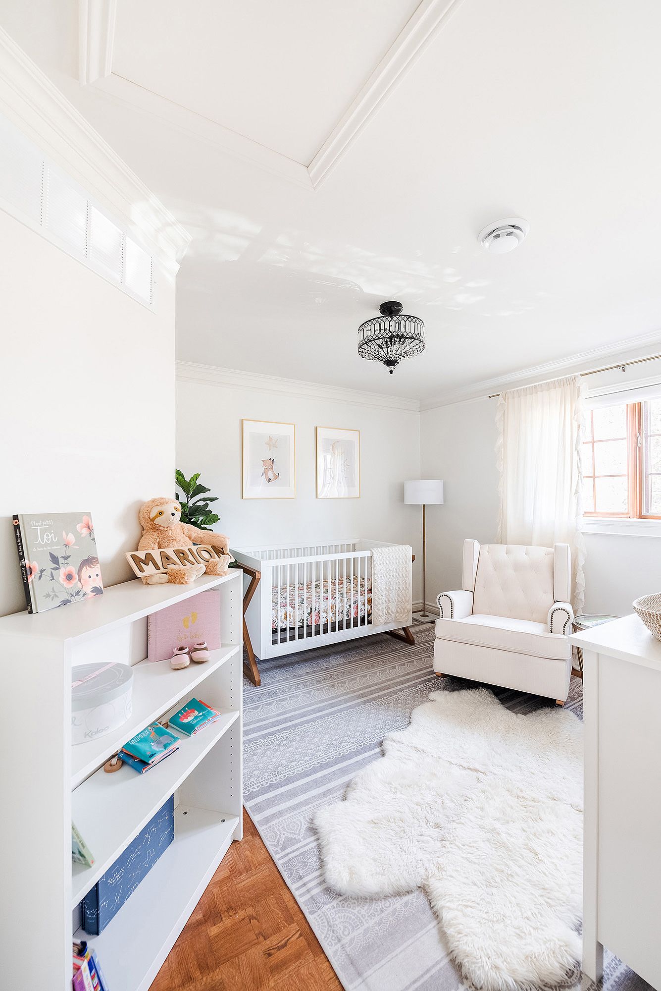 Bright white nursery room with crystal chandelier, white crib, and plush area rug on hardwood floors.