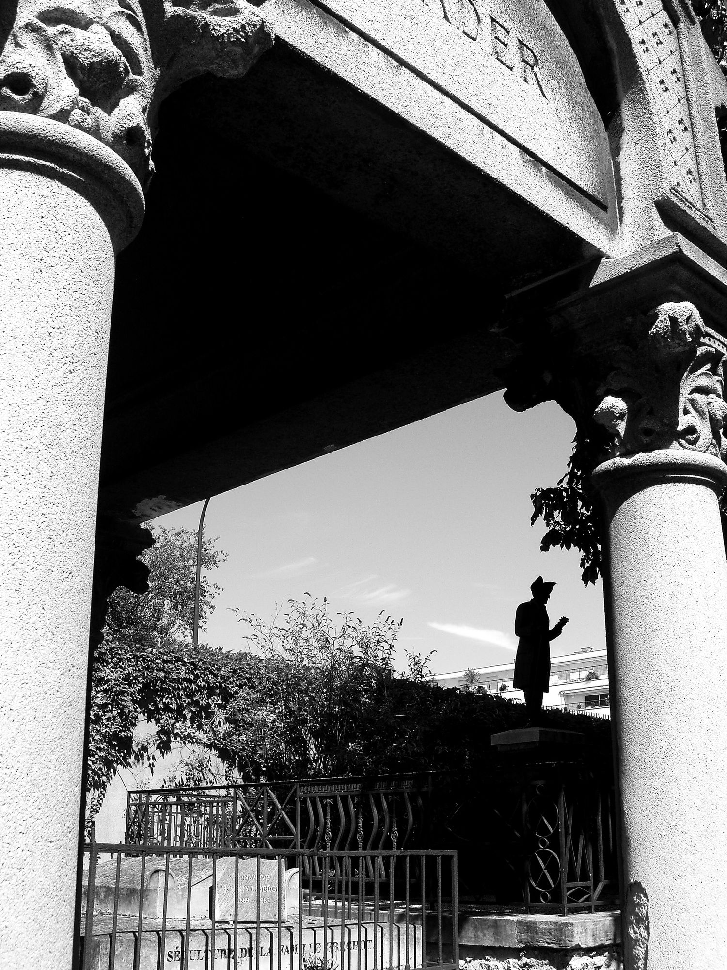 Architectural detail of white columns and ornate capitals against bright sky with fence in background.