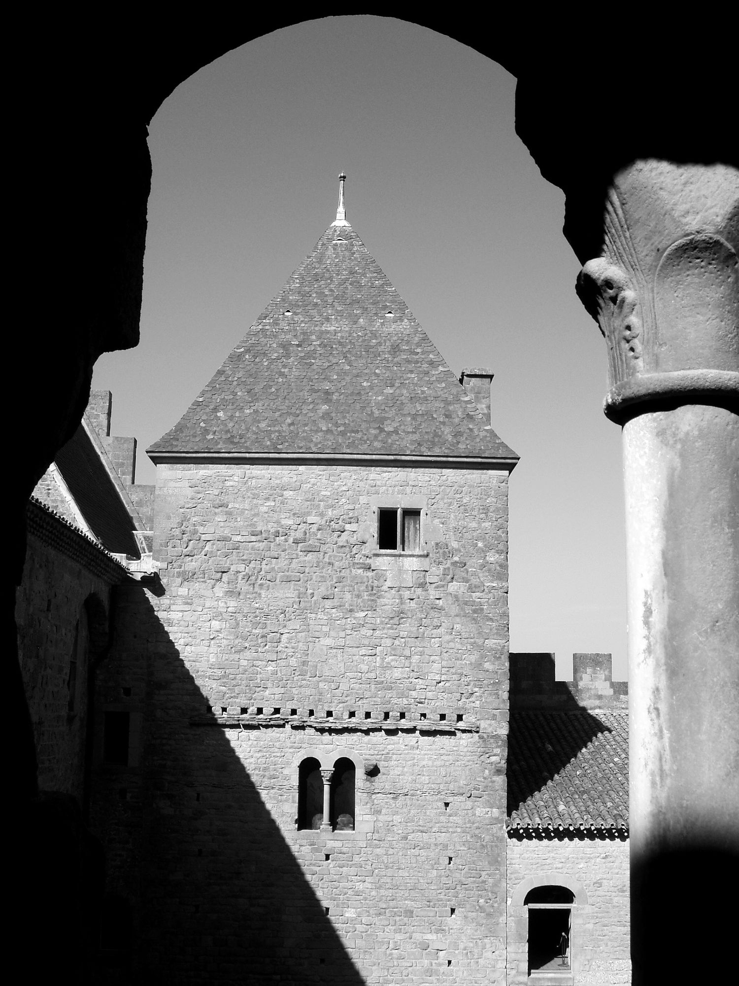 Historic stone tower photographed through architectural arch in monochrome.