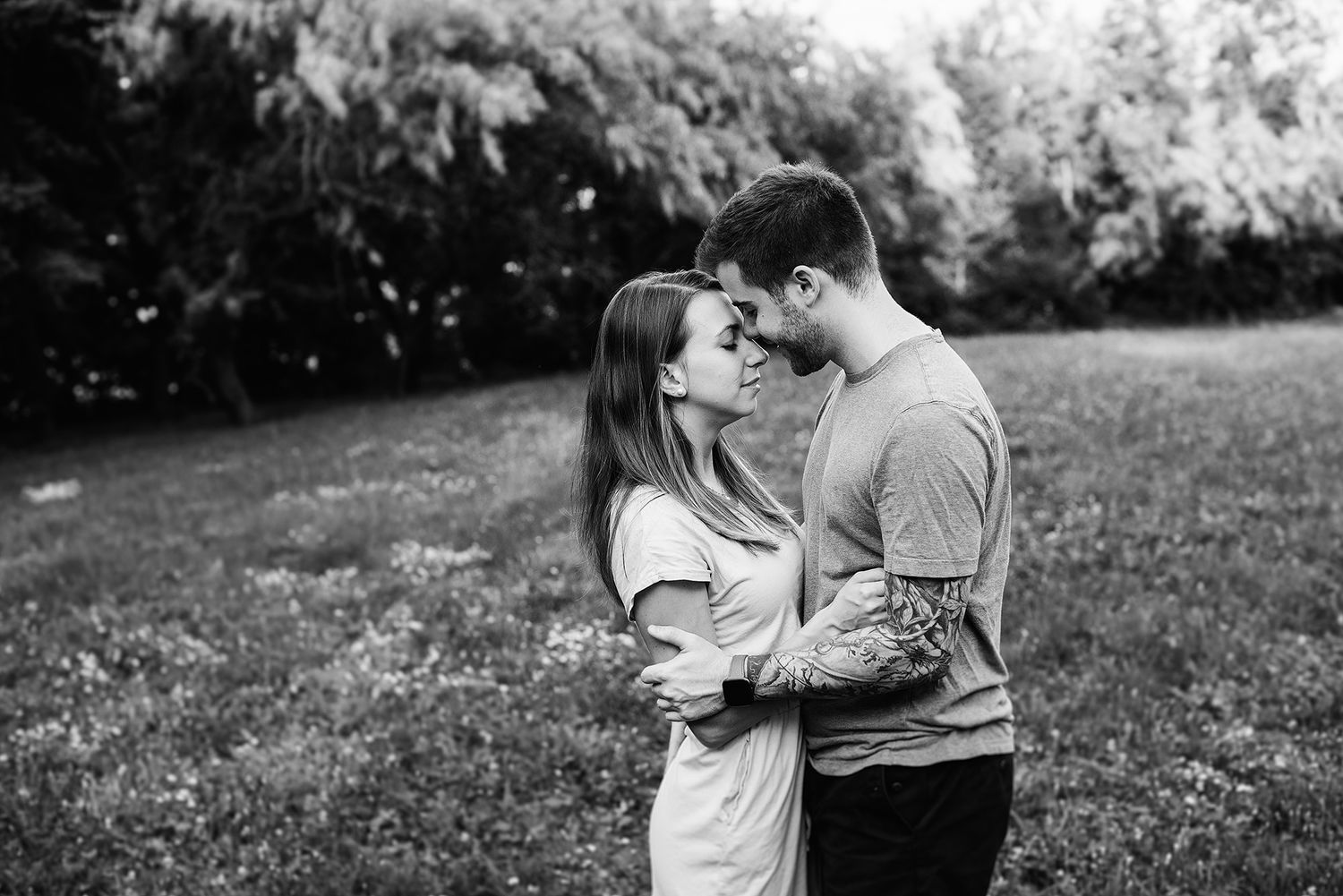 An intimate black and white portrait of a couple sharing a tender moment outdoors.