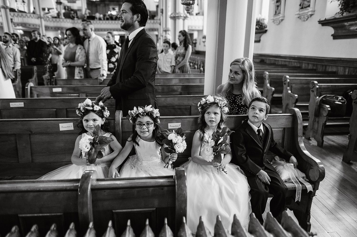 Black and white photo of young children sitting in church pews during a wedding ceremony wearing formal attire.