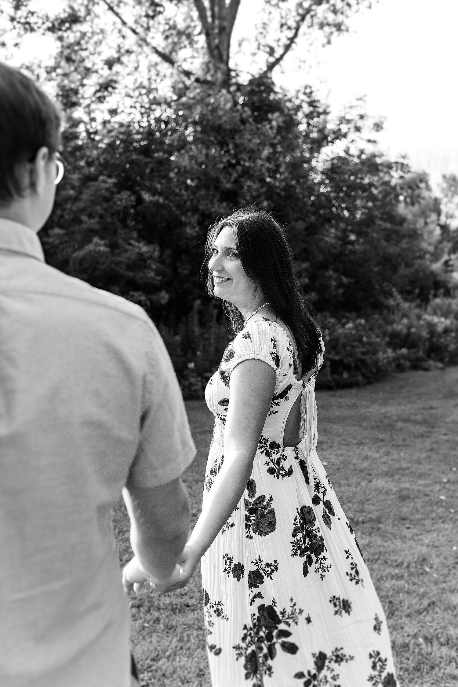 A couple holding hands and walking together in a park, with the woman wearing a floral dress.
