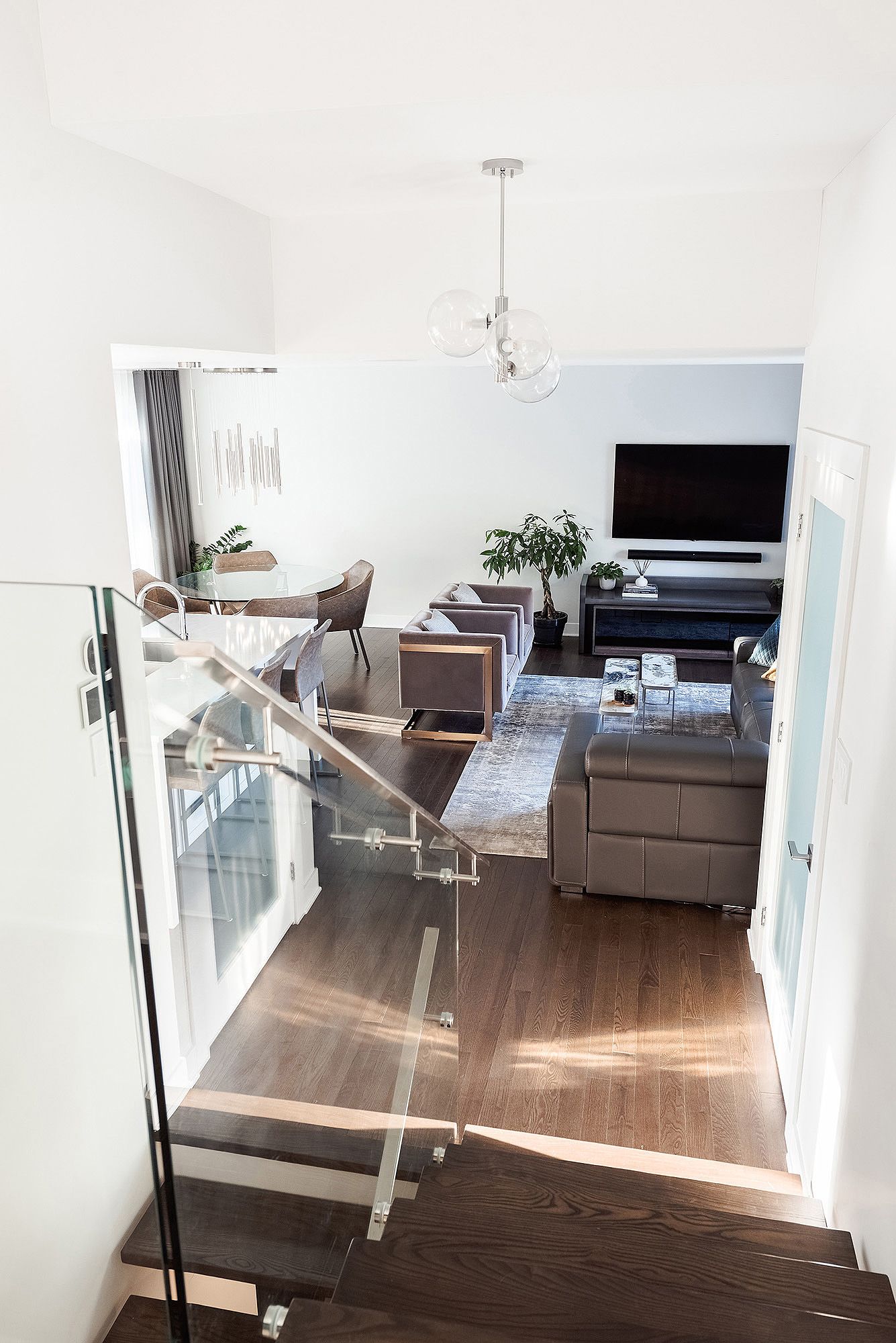 Modern open concept living room with hardwood floors and glass railings in a bright white space.