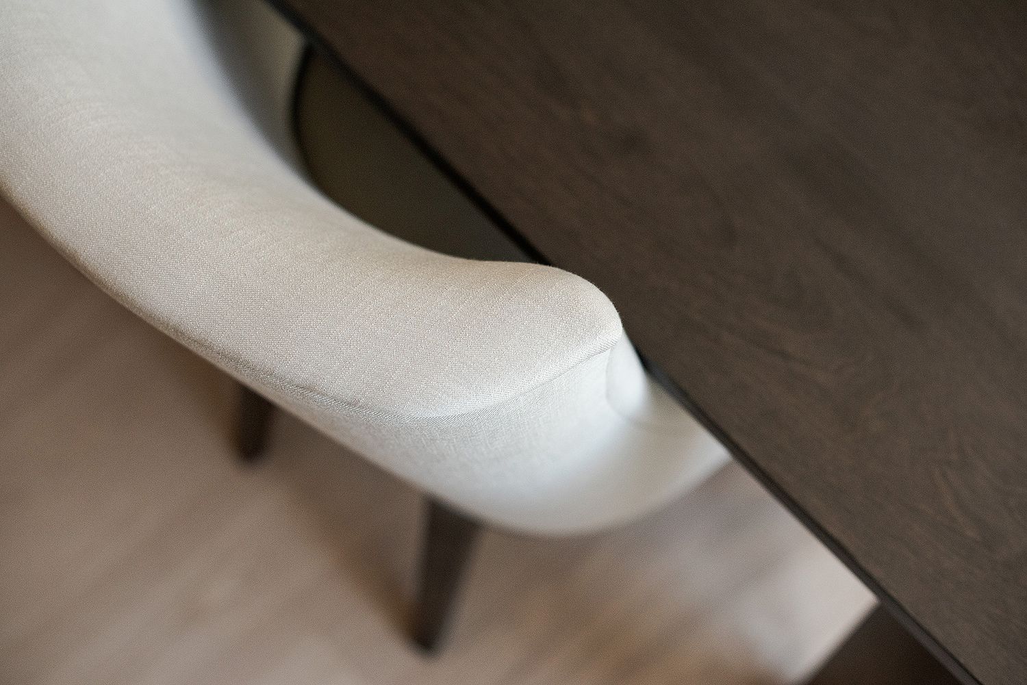 Close-up view of a curved white chair arm against dark flooring.