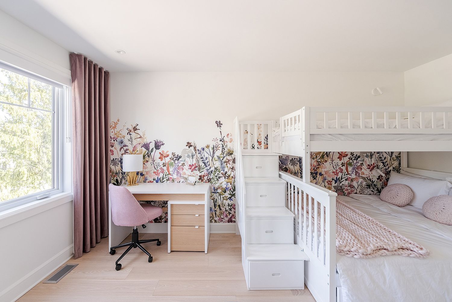 A serene nursery room with white furniture, floral wallpaper, and natural light streaming through large windows.