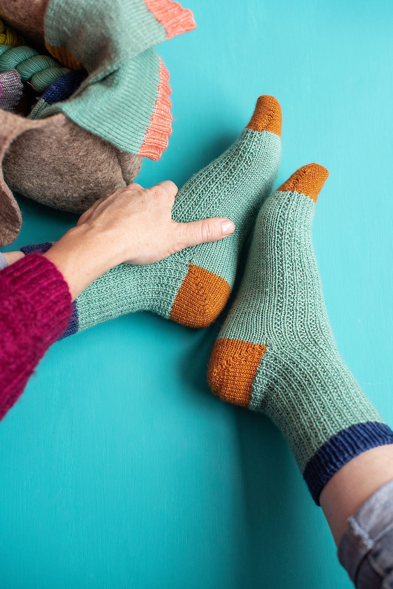 Close-up of mint green knitted socks with orange accents being worn against turquoise background.