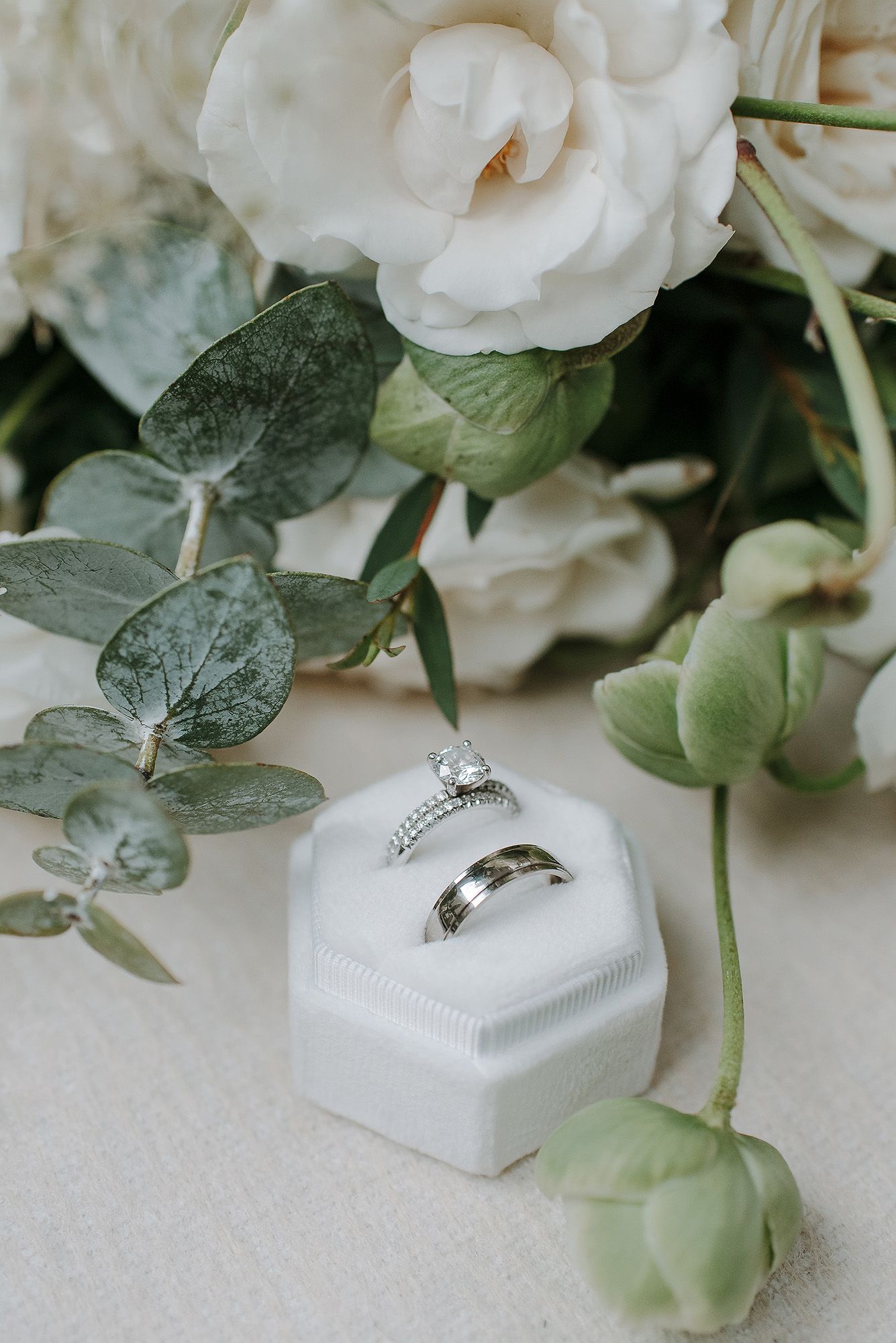 Wedding rings displayed on white ring boxes surrounded by delicate white flowers and green eucalyptus leaves.