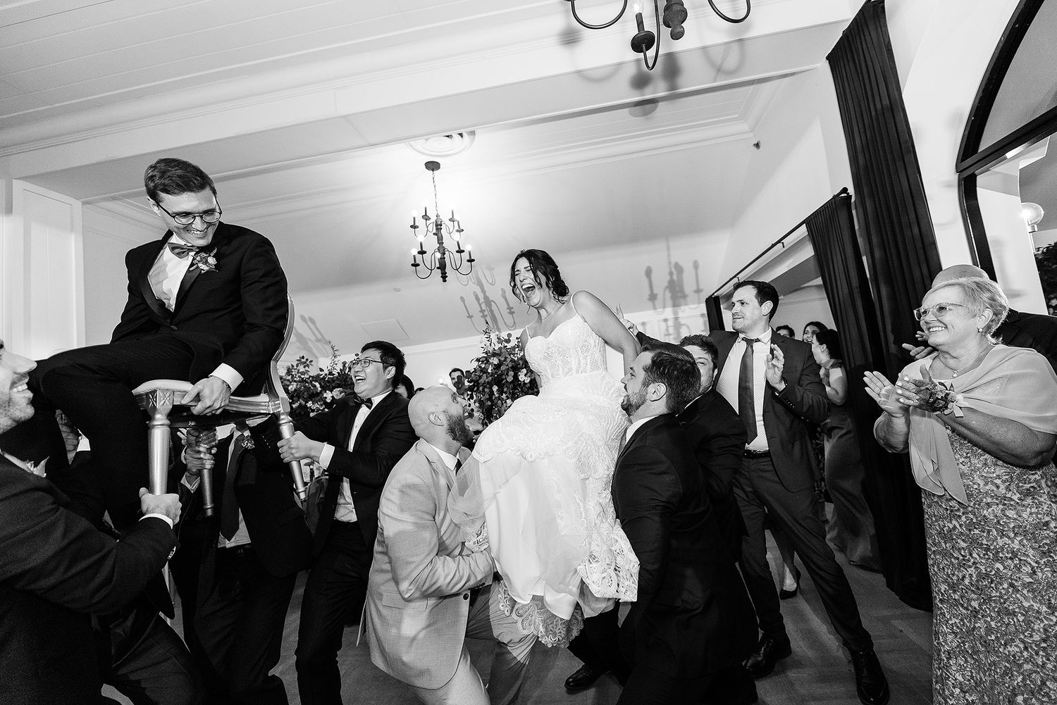 Black and white photo of wedding guests lifting and celebrating during a lively dance floor moment.