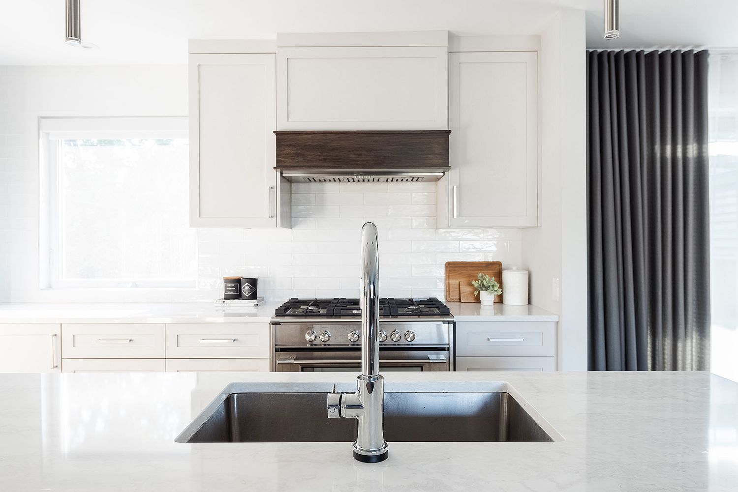 Modern white kitchen interior with quartz countertops, dark cabinets and stainless steel appliances.