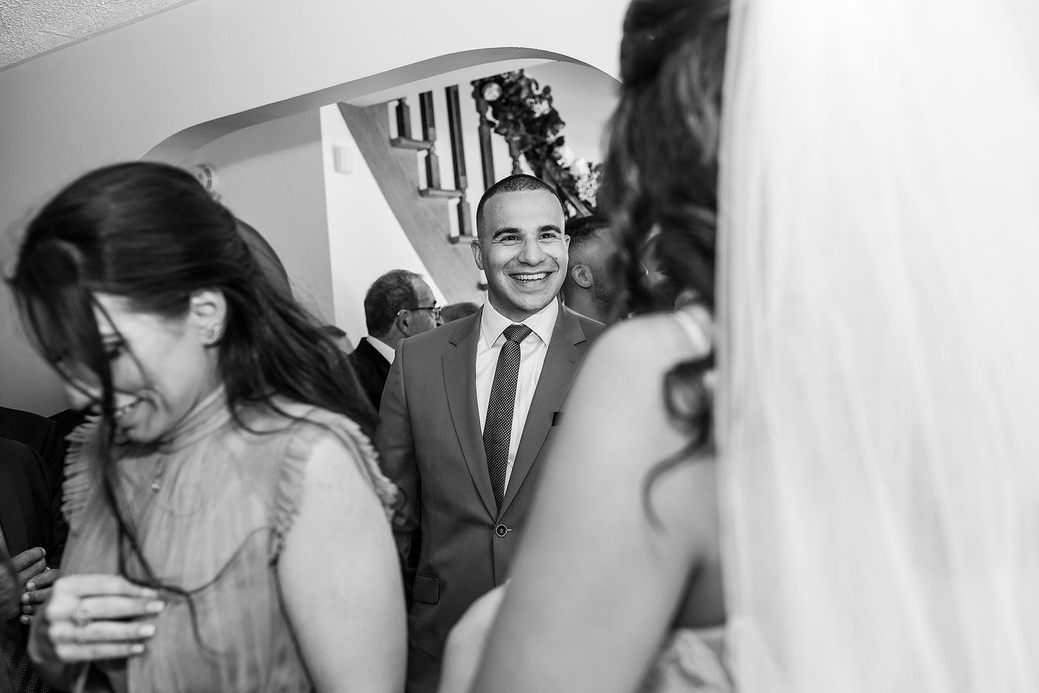 Black and white candid photo of wedding guests mingling at an indoor reception.