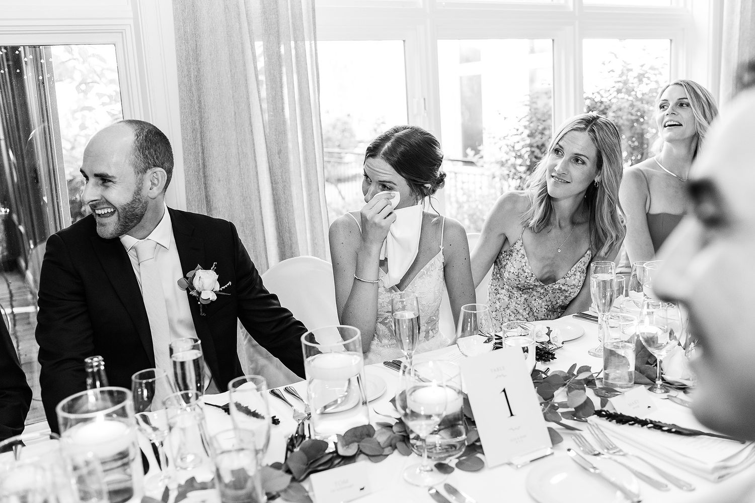 Black and white panoramic photo of wedding guests seated at long tables during a reception celebration.