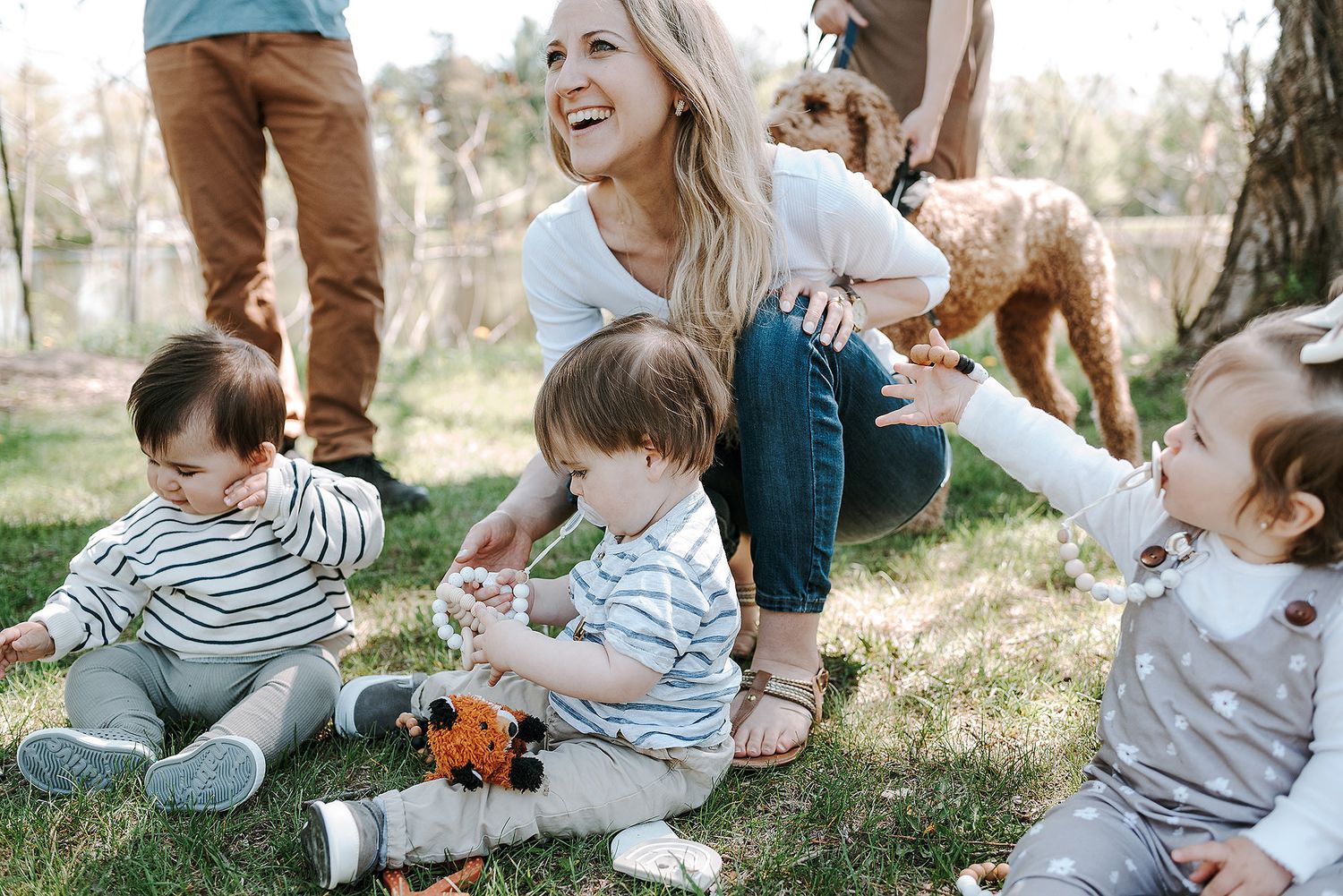 Multiple families relaxing on grass during outdoor social meetup with their children.