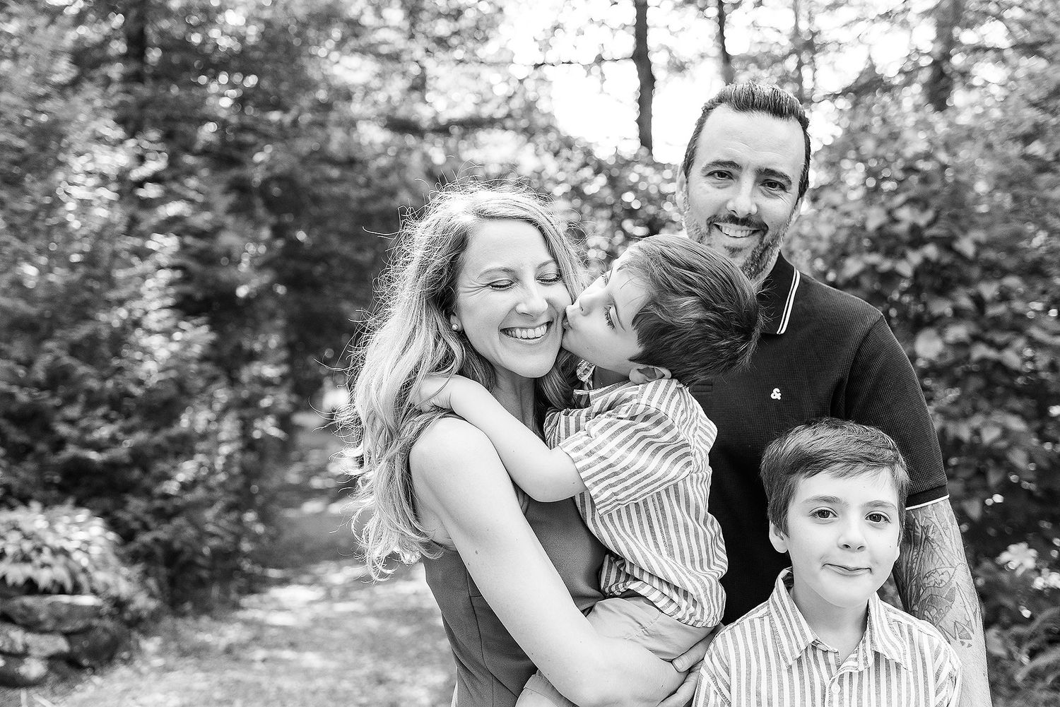 Family enjoying a playful moment together in a wooded outdoor setting during a photo session.