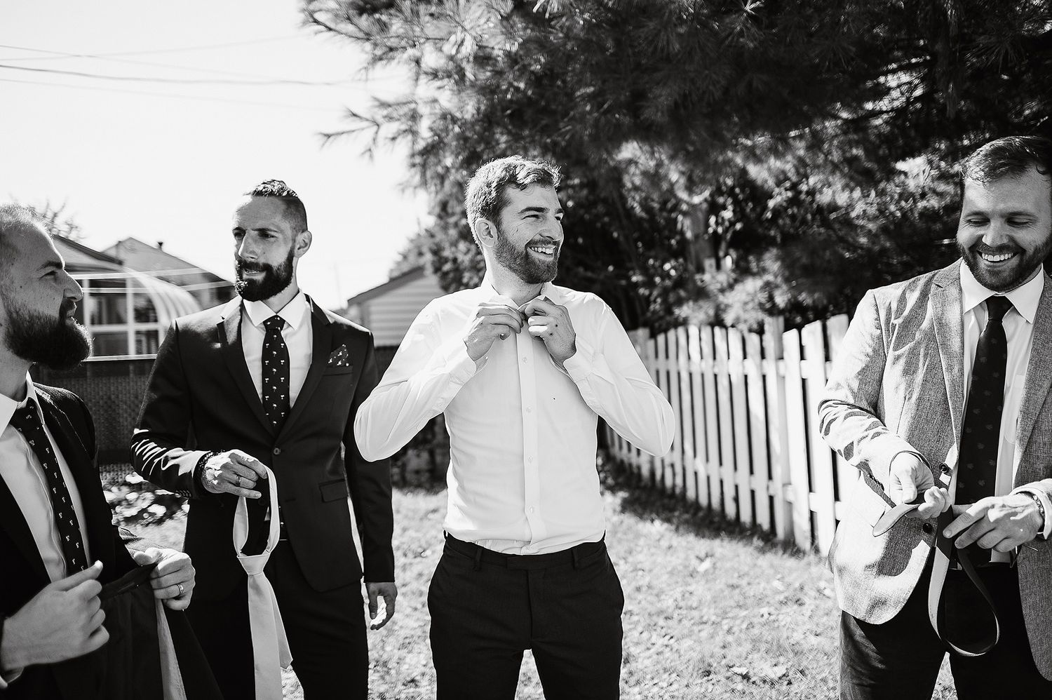 Wedding party members laugh and celebrate together outdoors in casual poses.