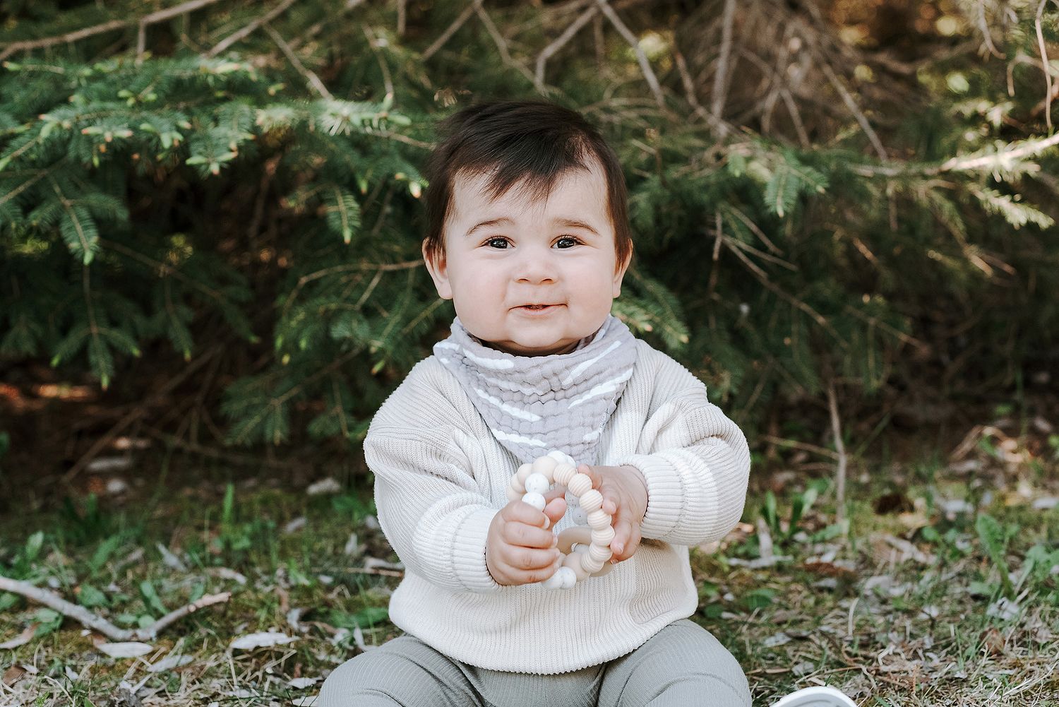 Baby in white sweater sitting on ground with a cheerful expression.