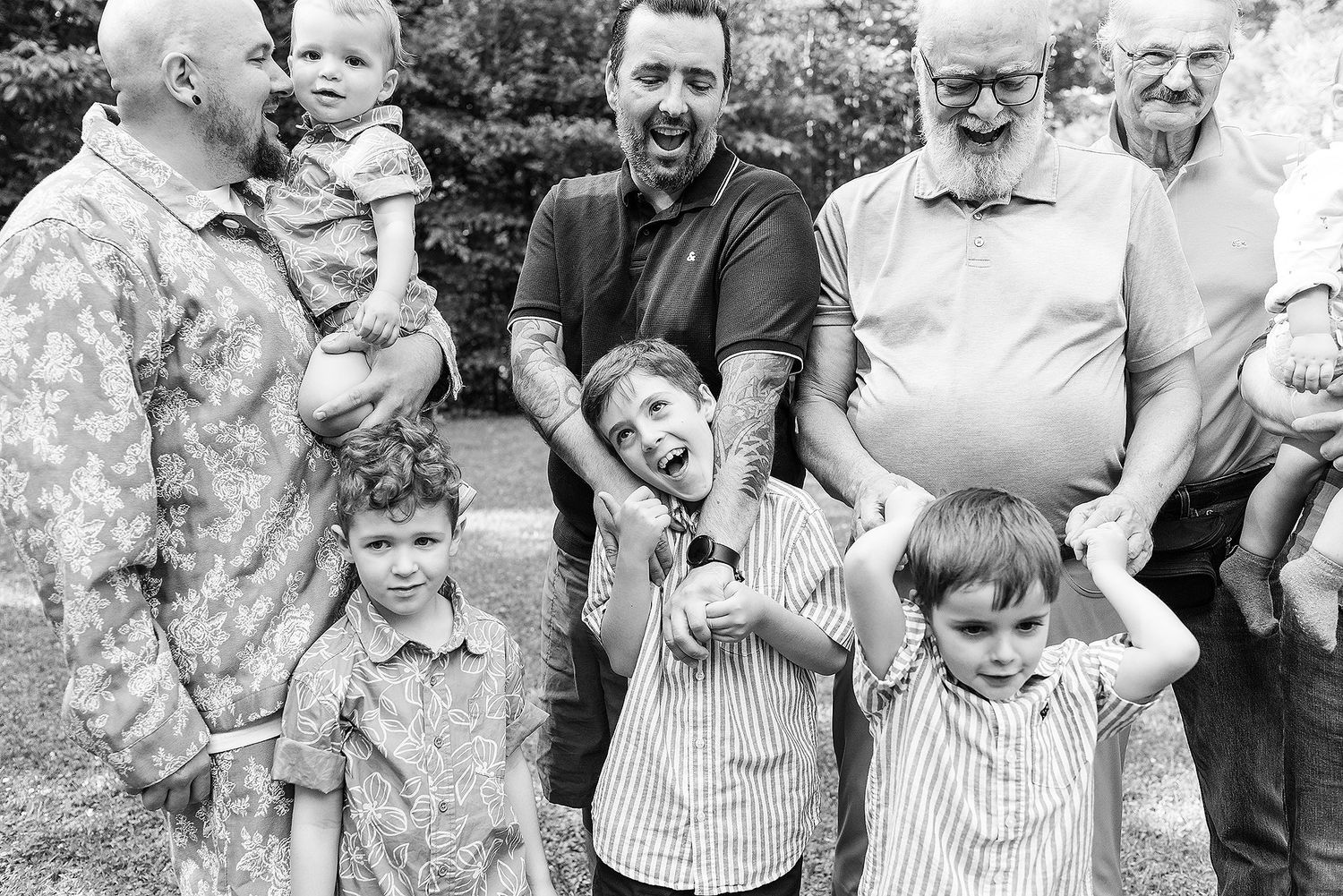 A joyful multi-generational family gathering outdoors with everyone smiling and laughing together in black and white.