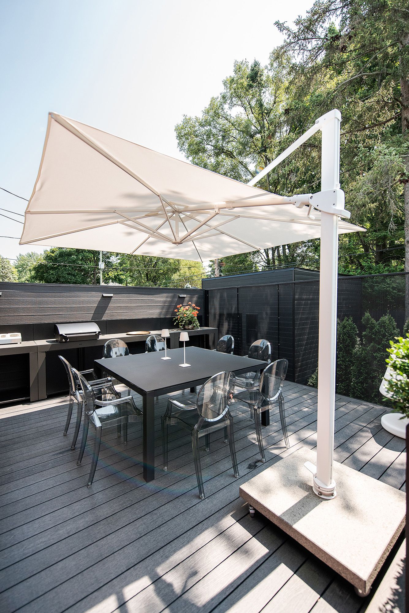 Modern outdoor deck with gray composite decking, white umbrellas, and dark dining furniture set in a backyard setting.