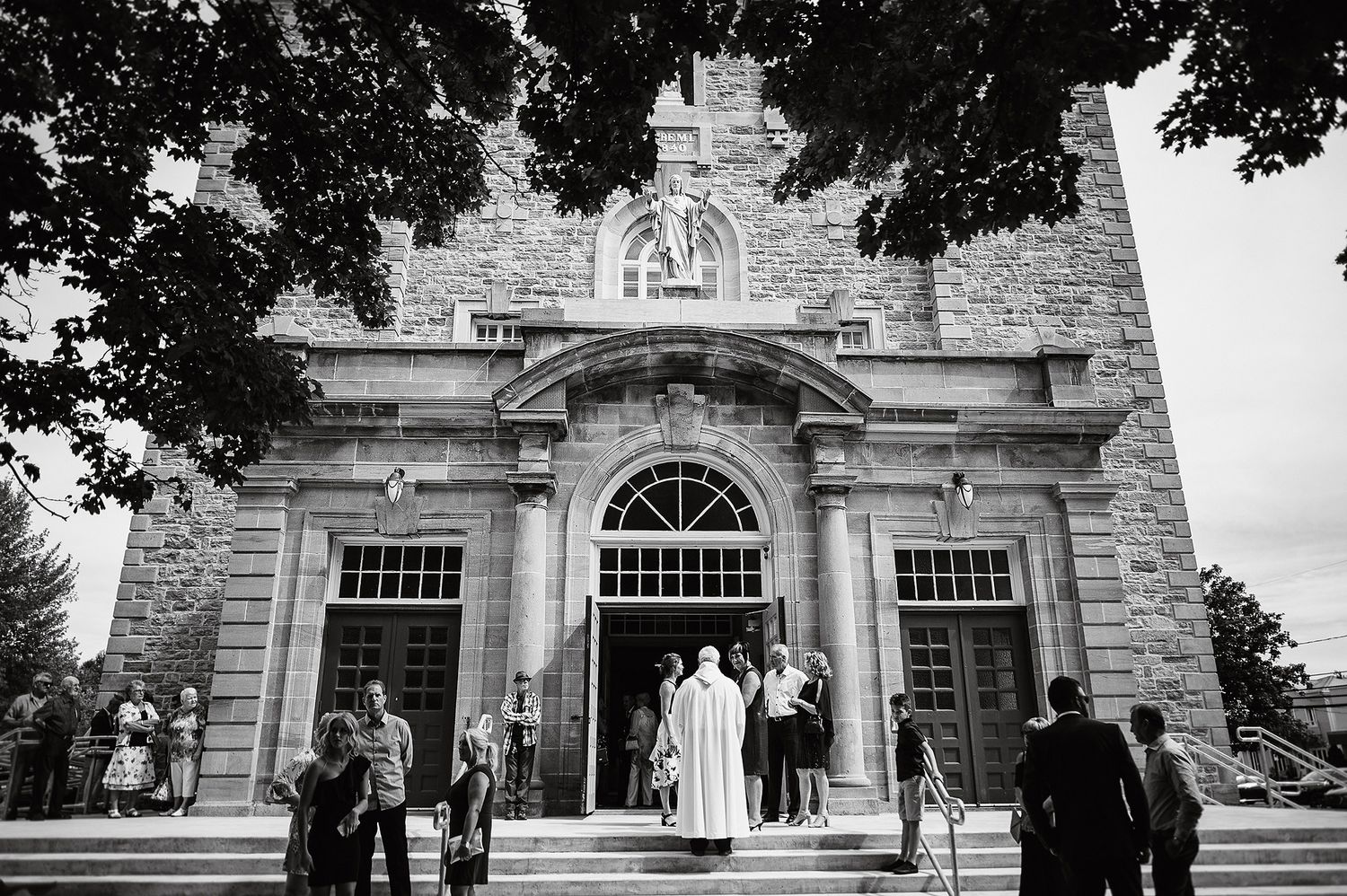 Black and white photos of wedding guests gathering outside a grand stone building with arched windows and columns.
