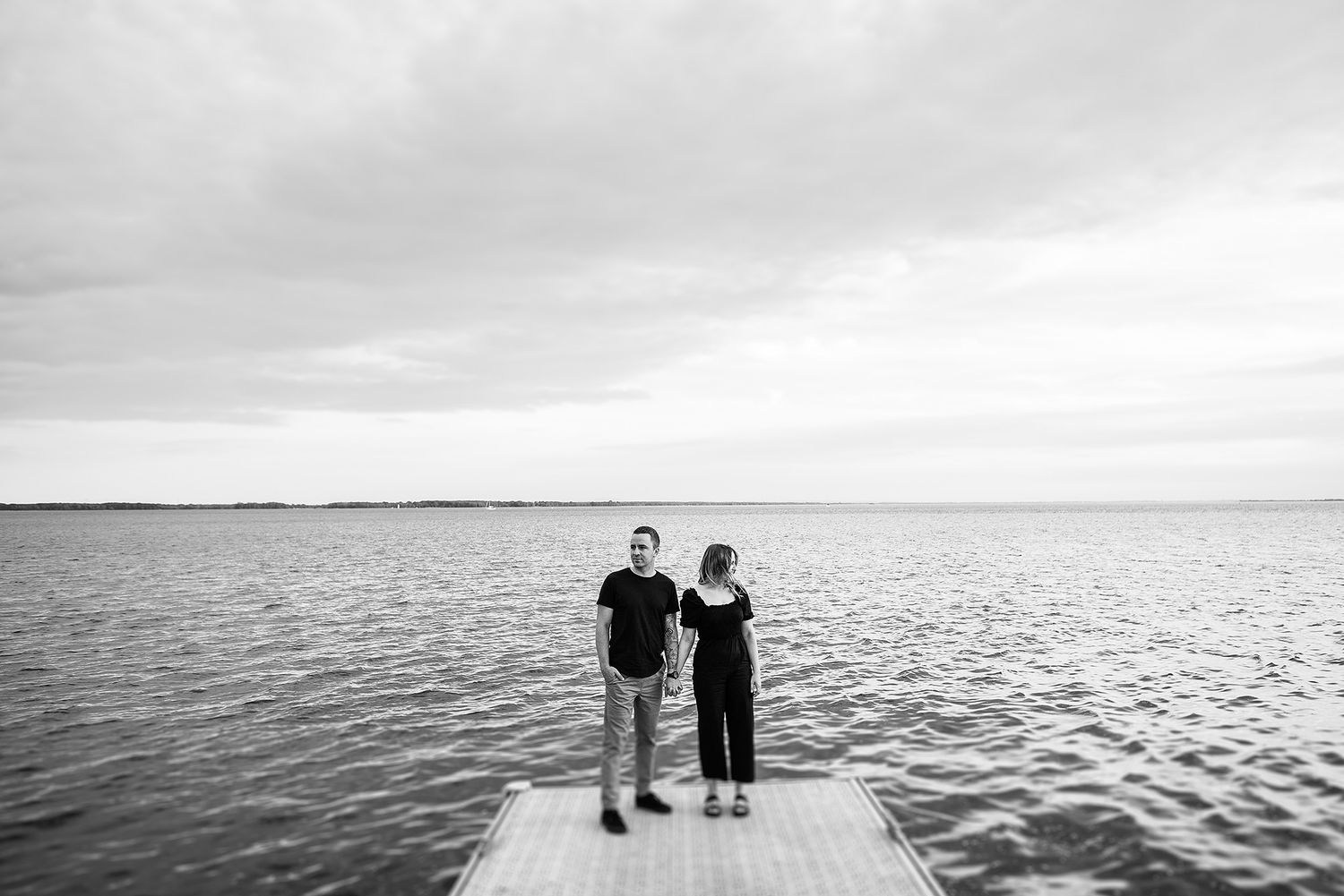 Couple standing together overlooking a vast lake under cloudy skies.