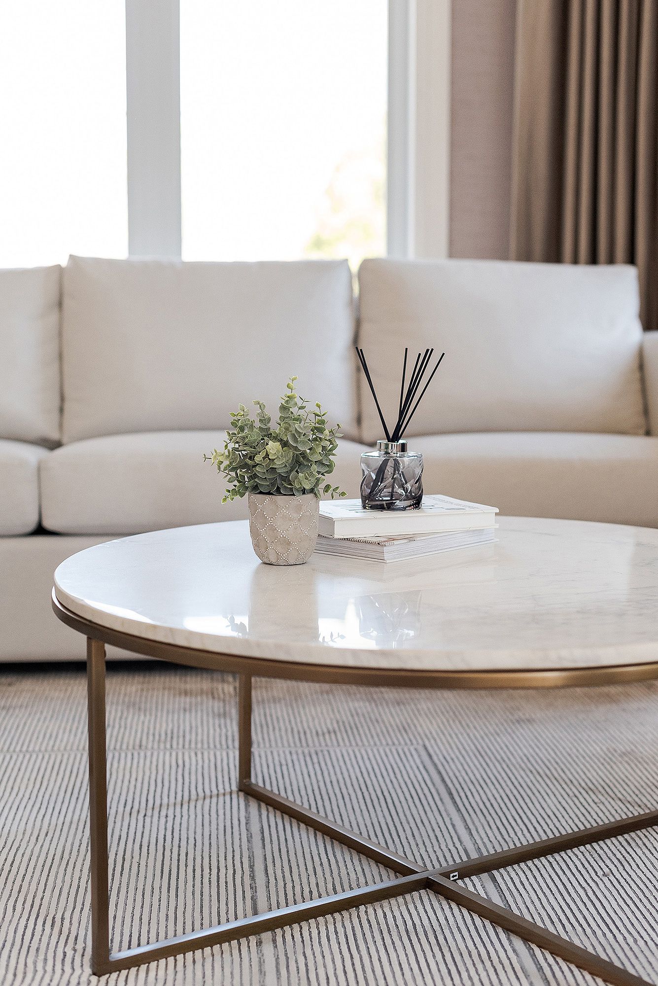 Modern round marble coffee table with metal base sits elegantly on a textured gray area rug in a minimalist living room.