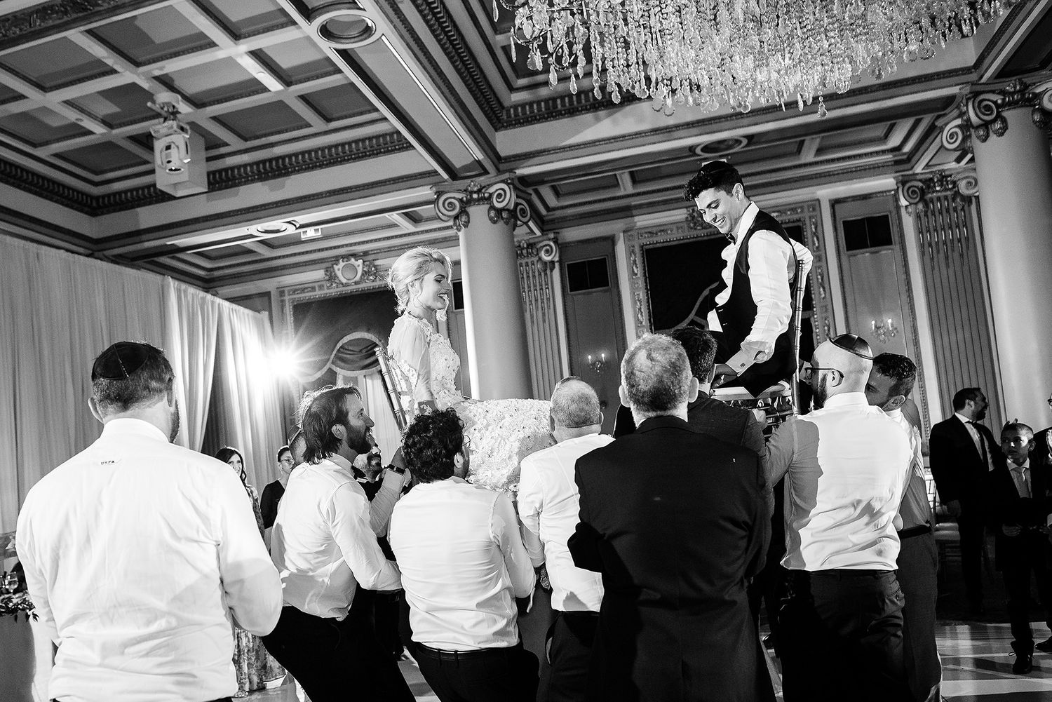 Black and white panoramic view of wedding guests dancing and celebrating at an elegant indoor reception.