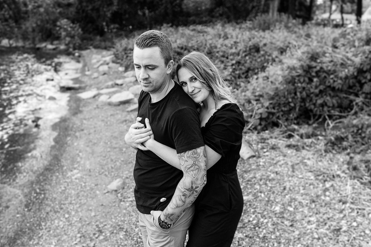 Couple sharing tender moments and embraces along a nature path in casual attire.